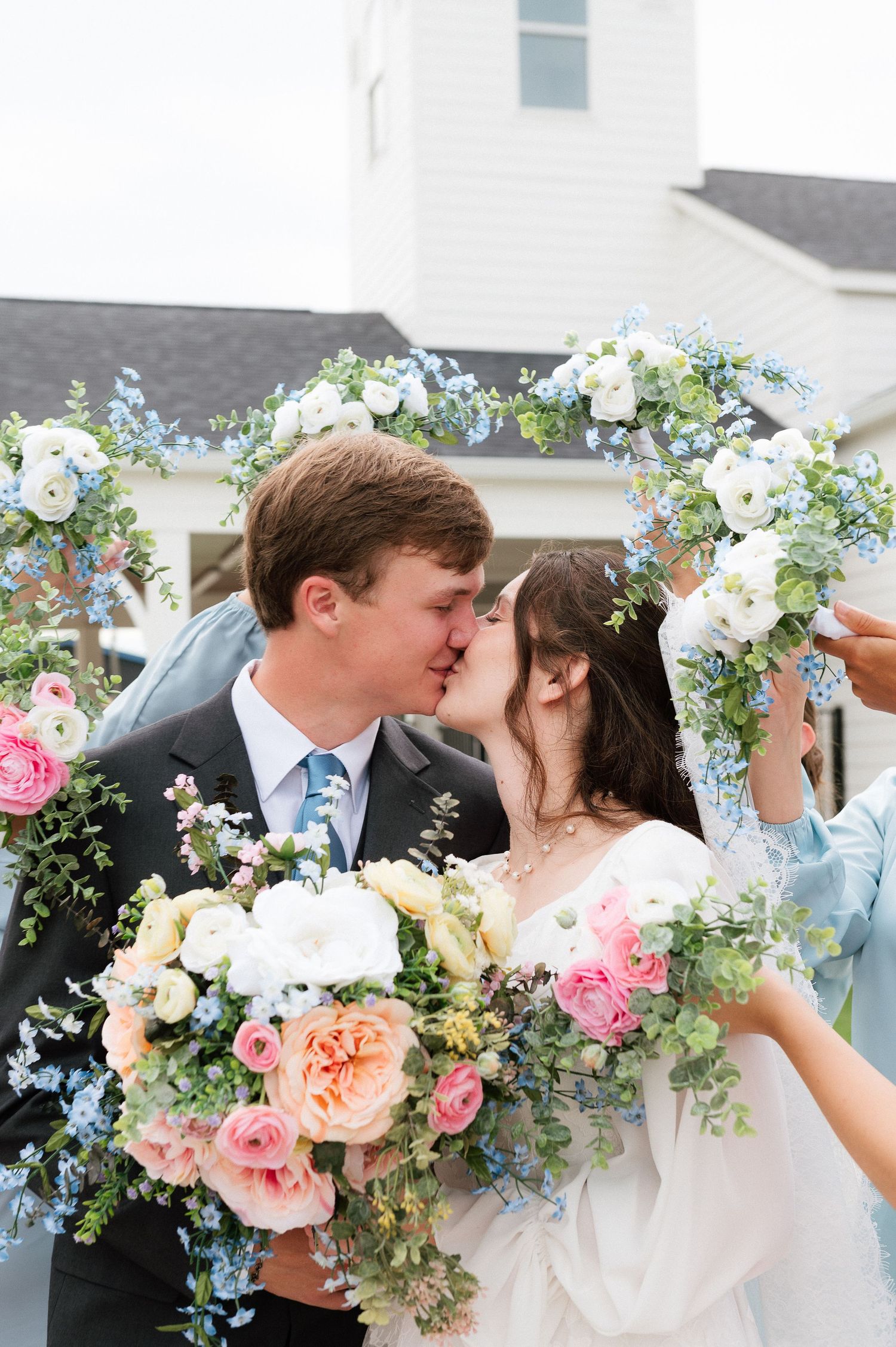 Bride and groom kissing through a floral hoop with white and blue flowers, bride holding a pink and white bouquet.