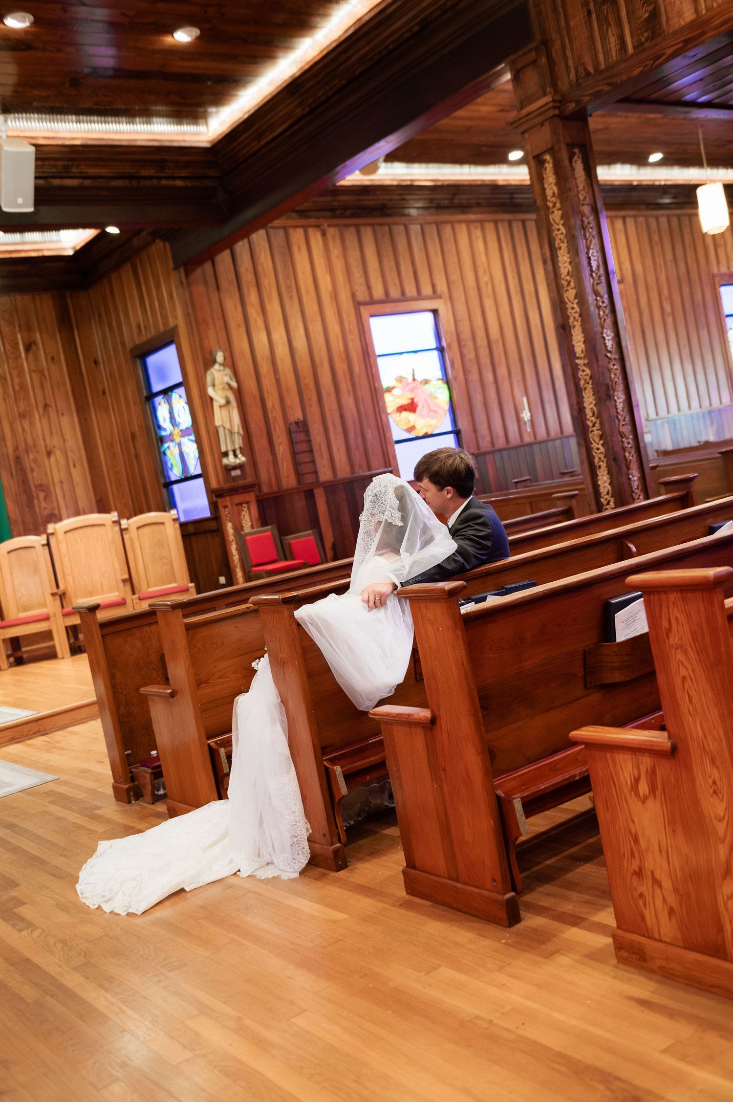 Bride and groom share a quiet moment praying together in wooden church pews on their wedding day.
