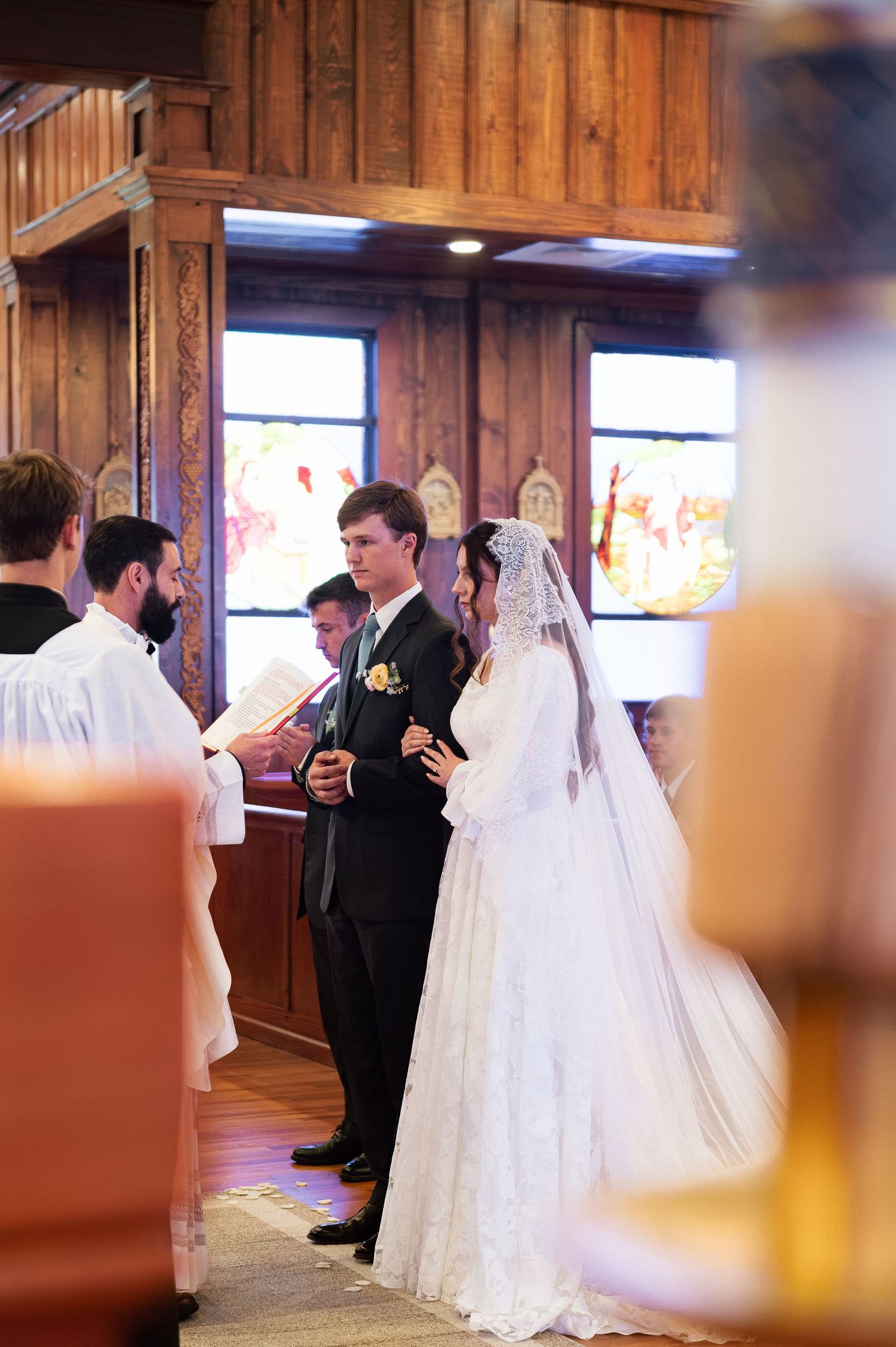 Bride and groom exchanging vows at a church wedding ceremony, with officiant reading from a book.