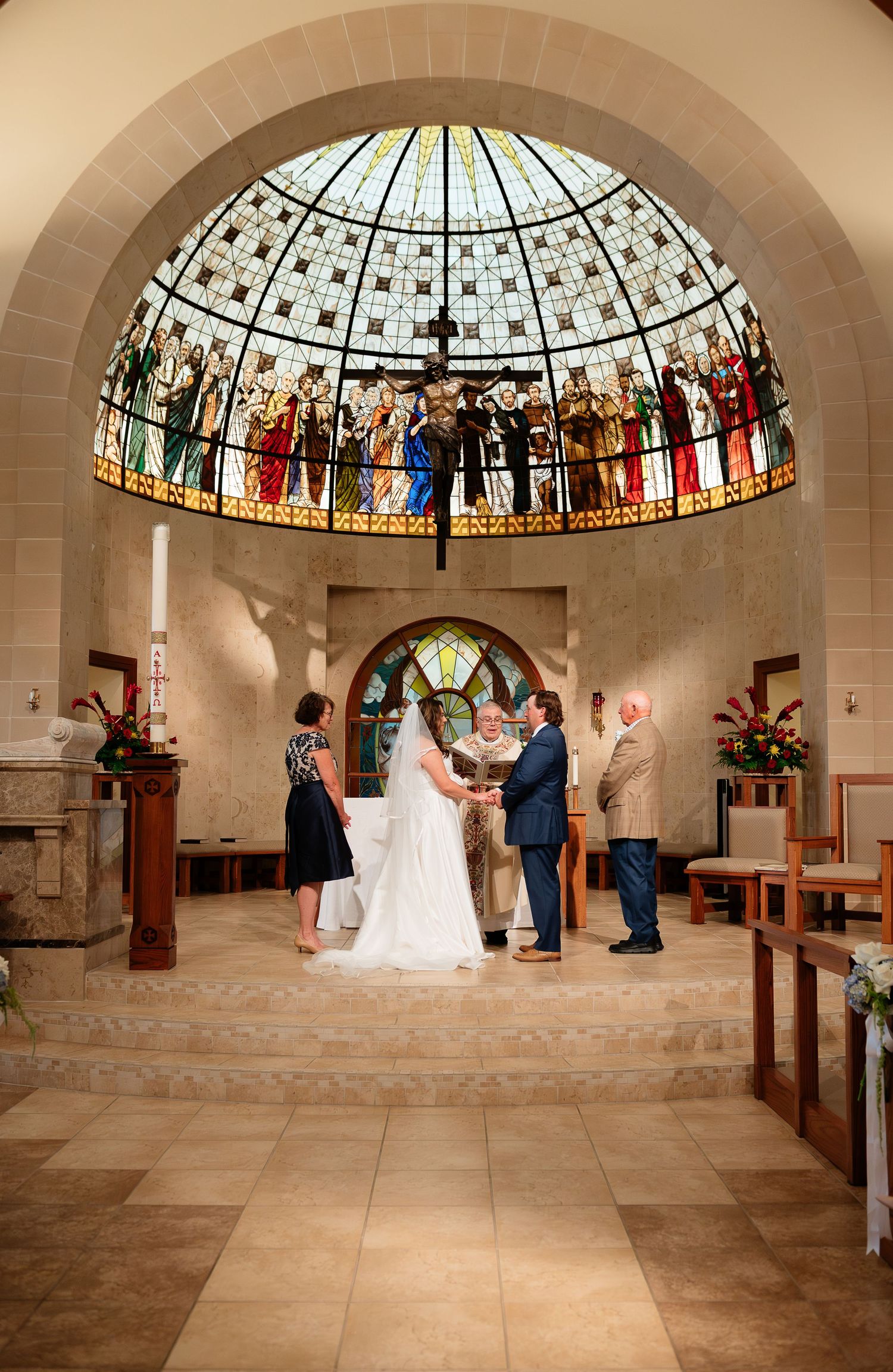 Wedding ceremony under stunning stained glass dome in elegant church with bride groom and officiant at altar.