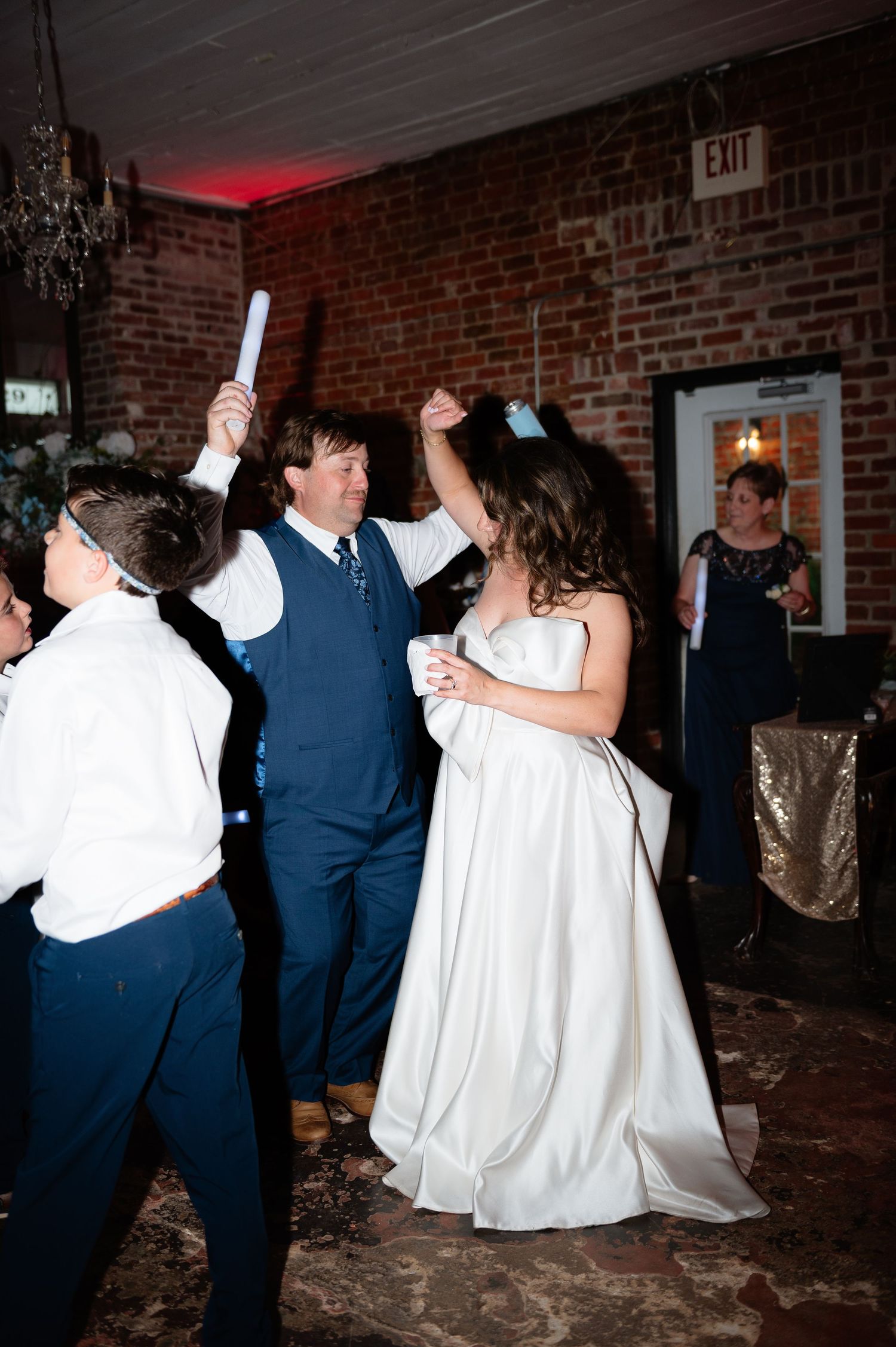 Bride and groom celebrate on wedding reception dance floor with guests holding glow sticks.