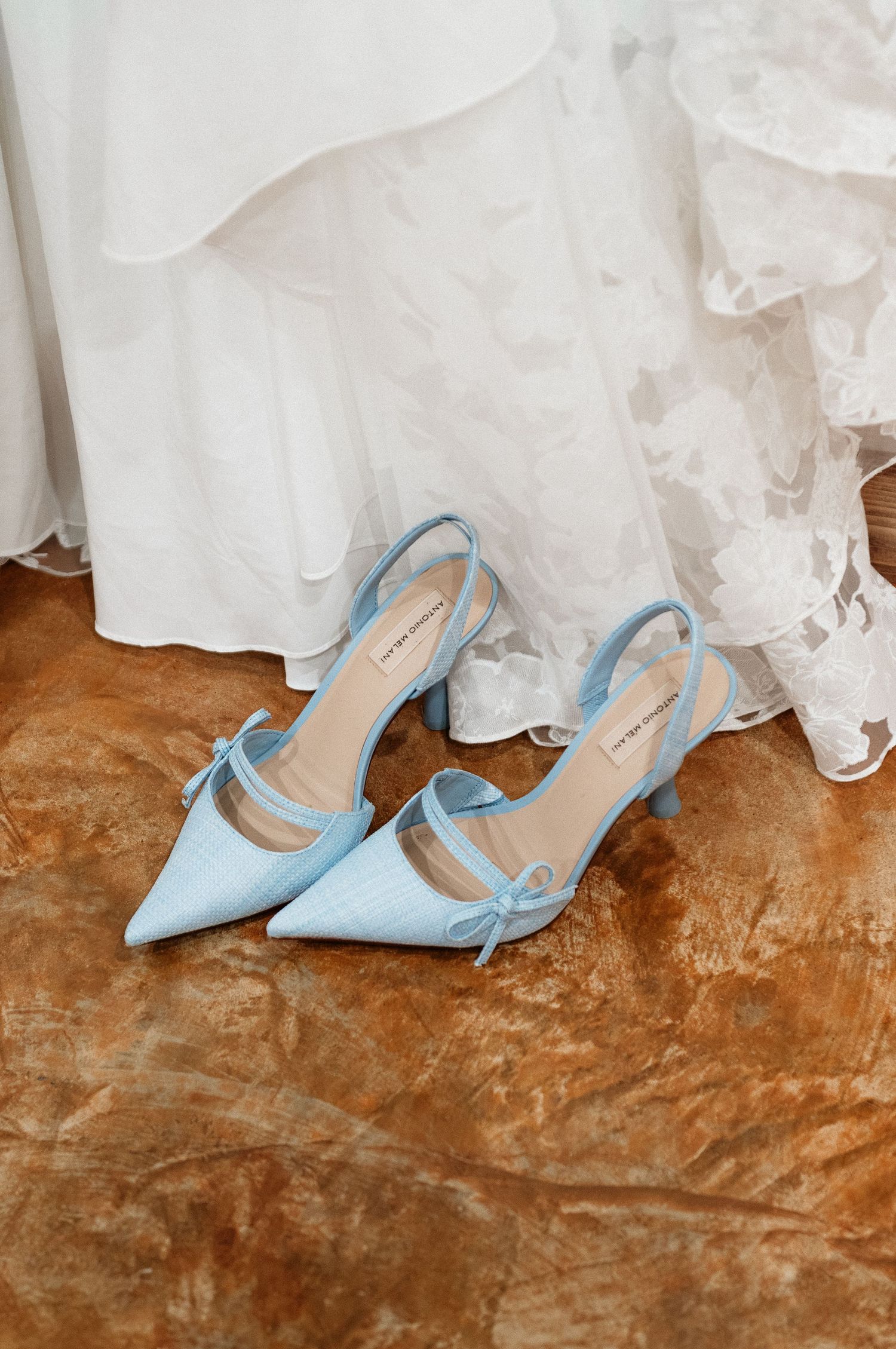Light blue satin kitten heel slingback pumps with bow detail placed in front of a white lace wedding dress.