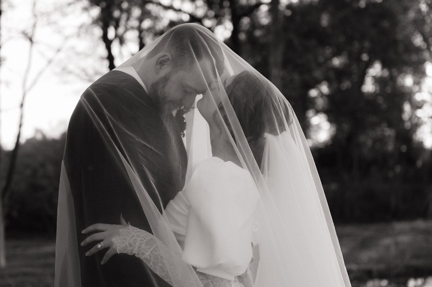 Romantic black and white wedding portrait with flowing veil creating soft movement.