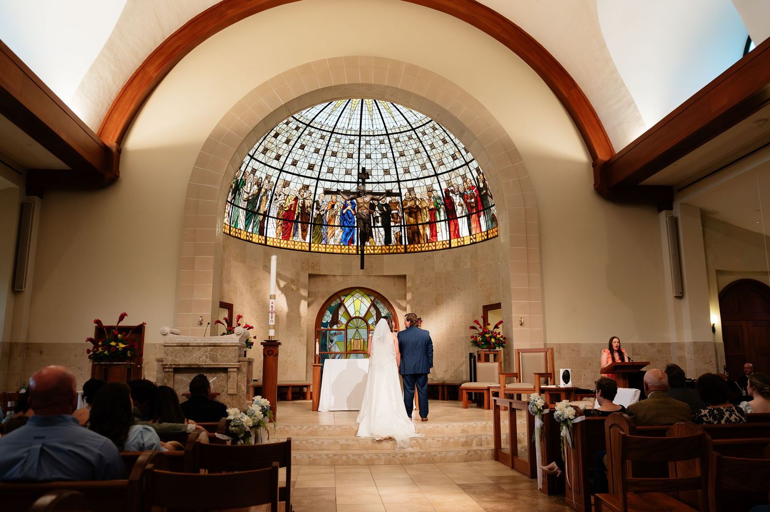 Couple exchanges vows at elegant church wedding ceremony beneath stunning stained glass dome and arched ceiling.