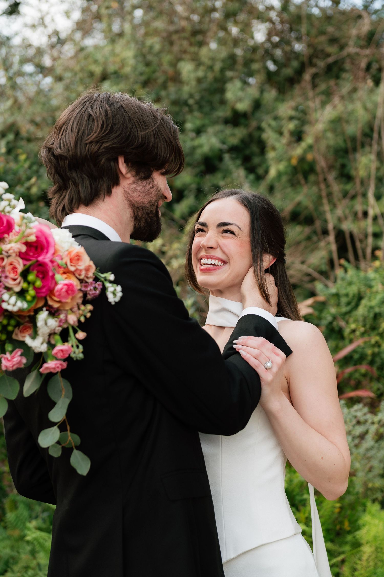 Couple sharing joyful moments among vibrant pink floral arrangements in a garden setting.