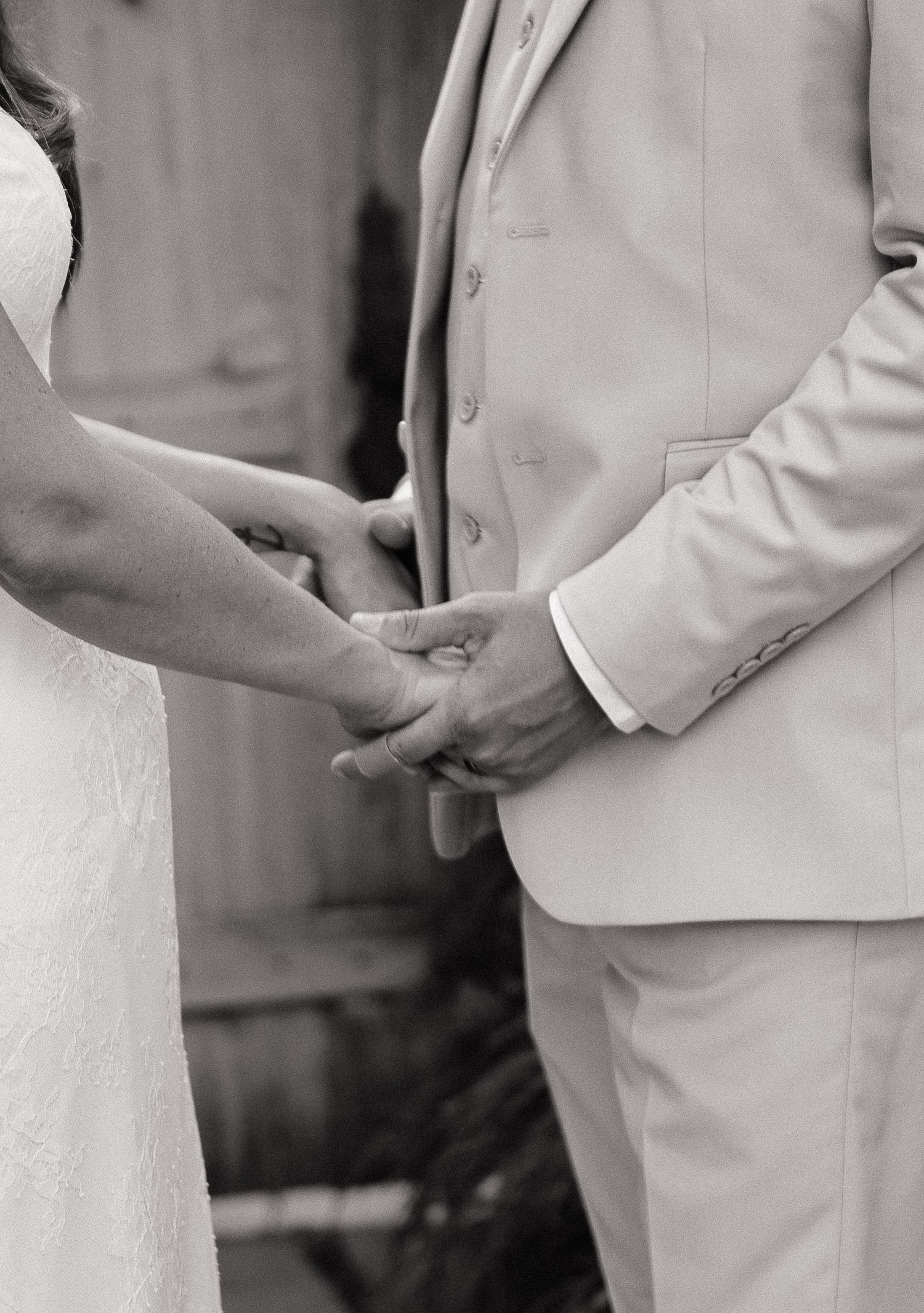 Black and white photo of a bride and groom holding hands during their wedding ceremony.