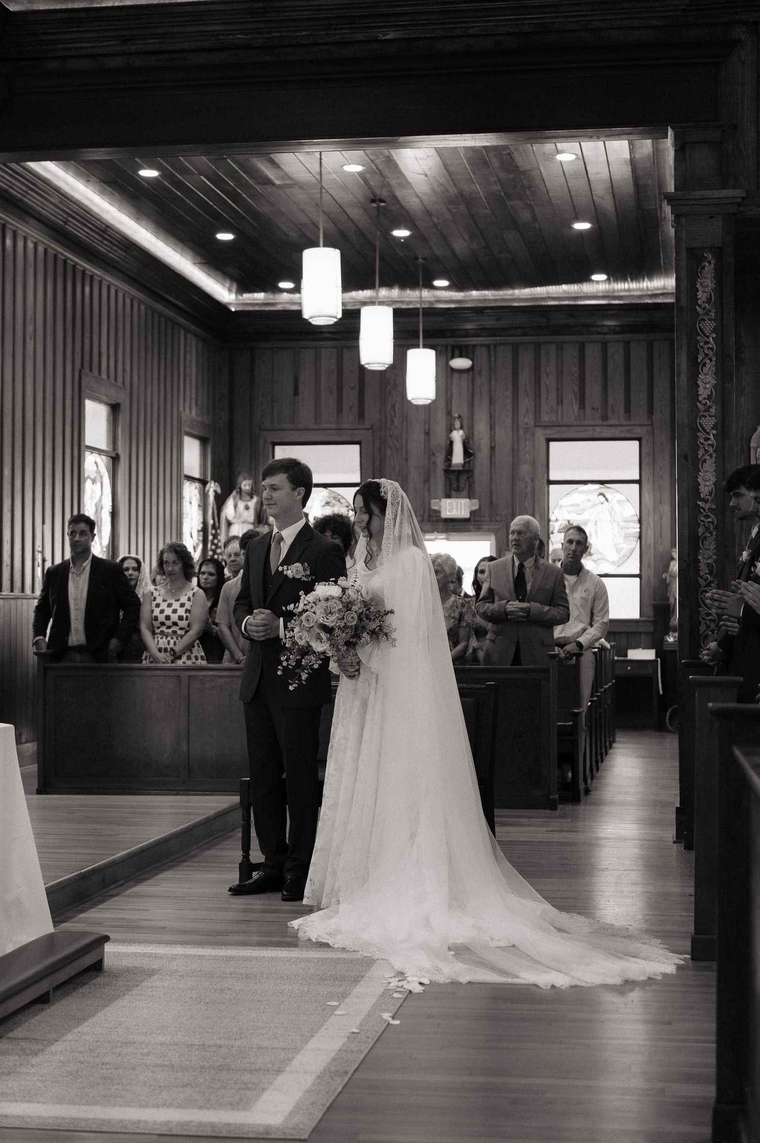 Black and white photo of a bride and groom walking down the aisle in a rustic wooden church during their wedding ceremony.