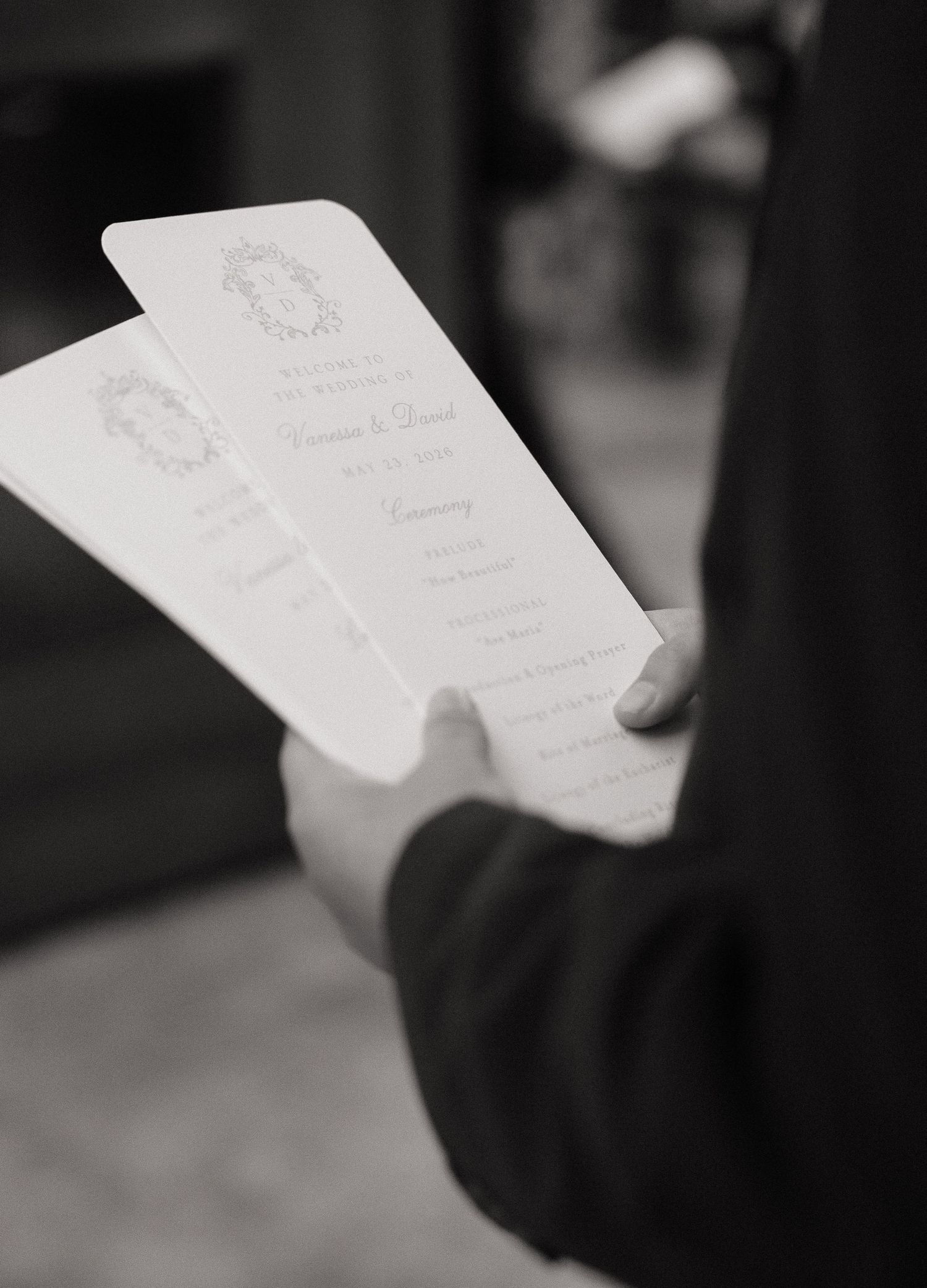Black and white photo of hands holding elegant wedding ceremony programs at a formal church wedding.