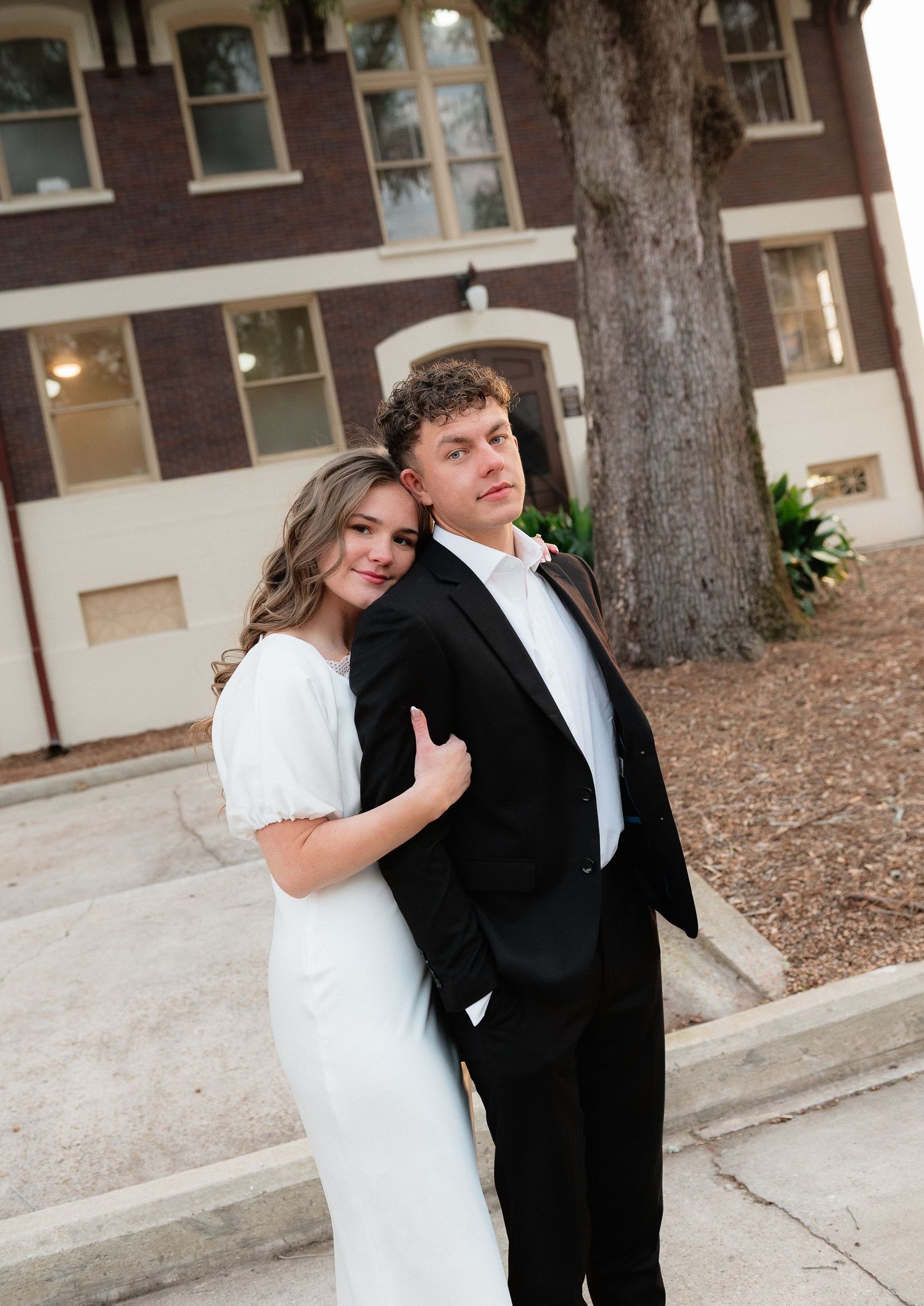 Wedding couple poses casually against an urban backdrop with fallen leaves on the ground.