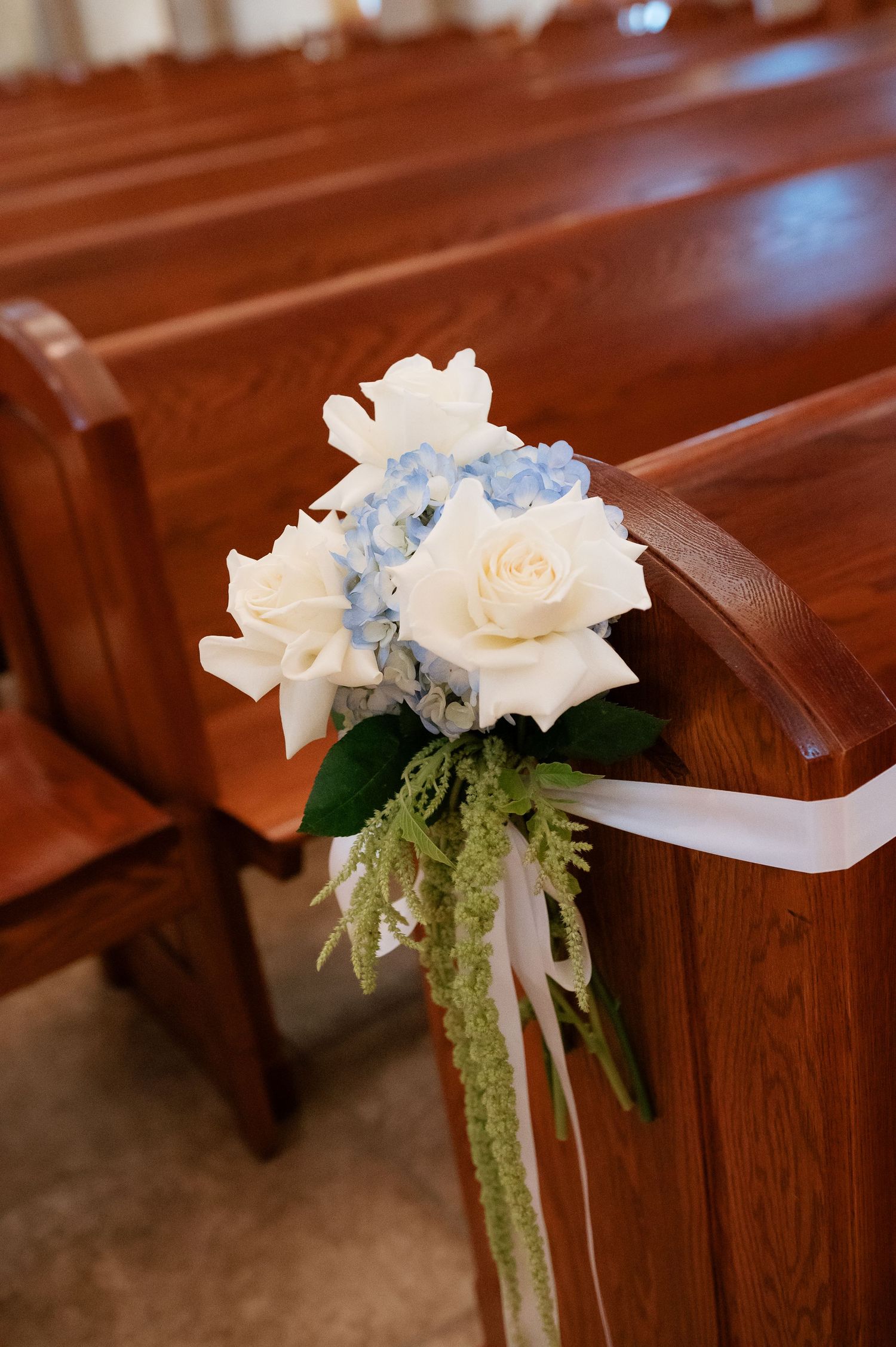 White roses and blue hydrangeas pew floral arrangement with green accents and white ribbon in a church.