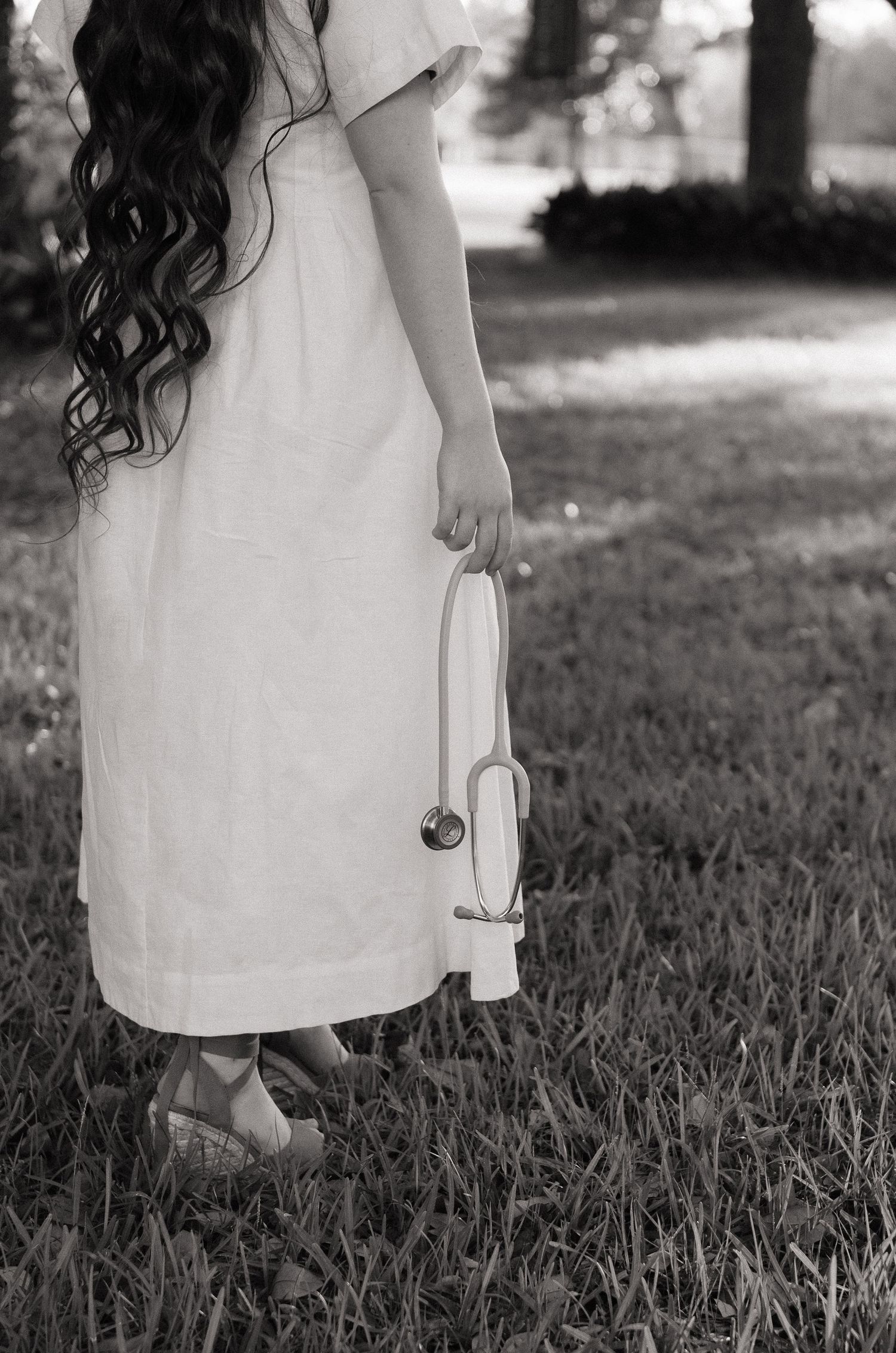 Black and white photo of a girl in white dress holding a stethoscope while standing on grass.
