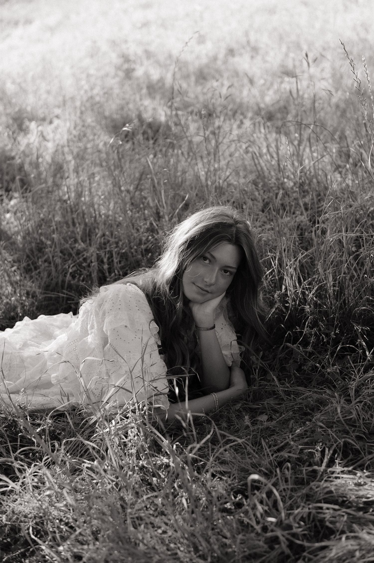Black and white photo of young woman lying in tall grass field, looking at camera.