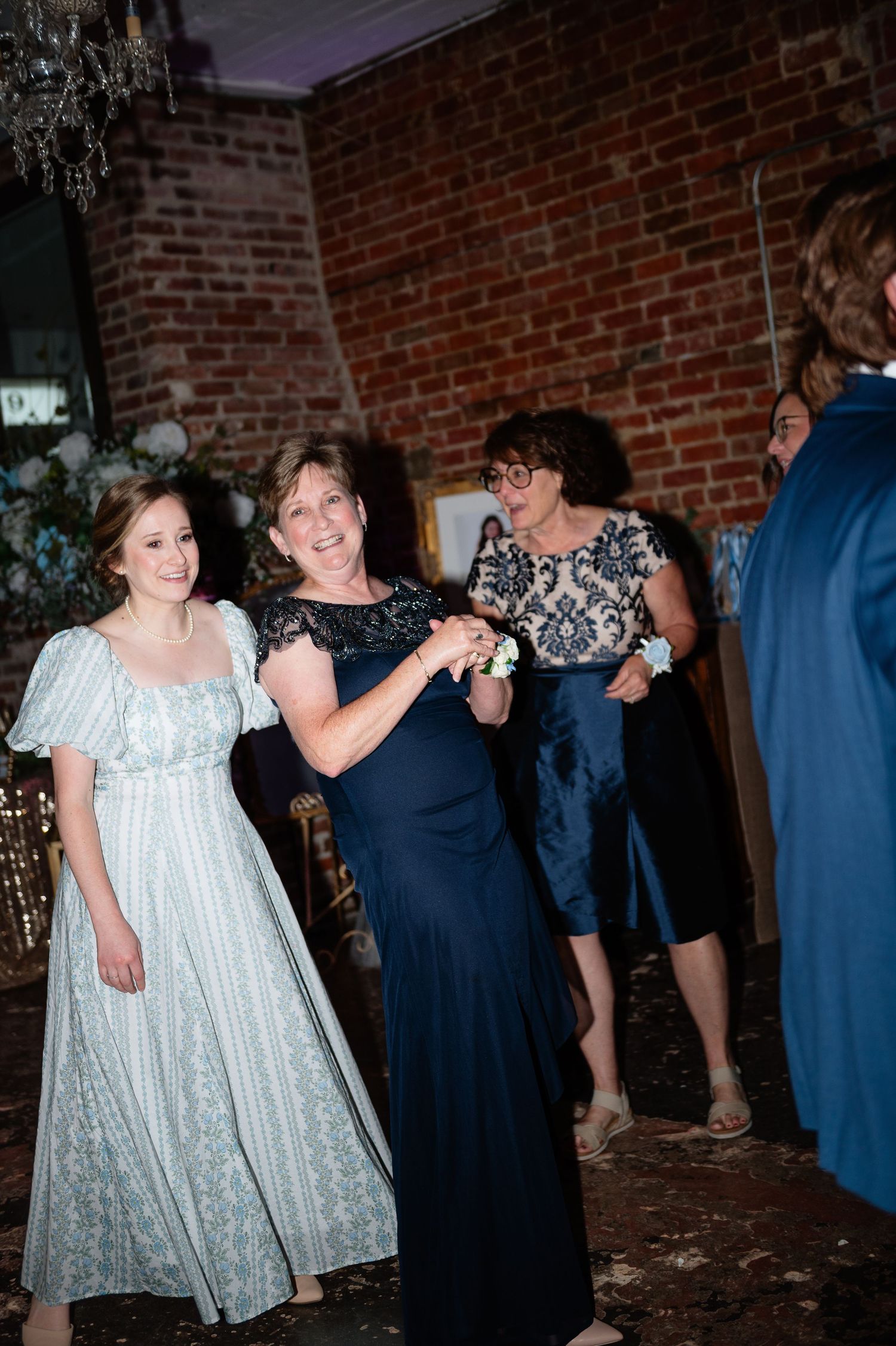 Guests in navy and mint dresses dancing and smiling at wedding reception in rustic brick venue.