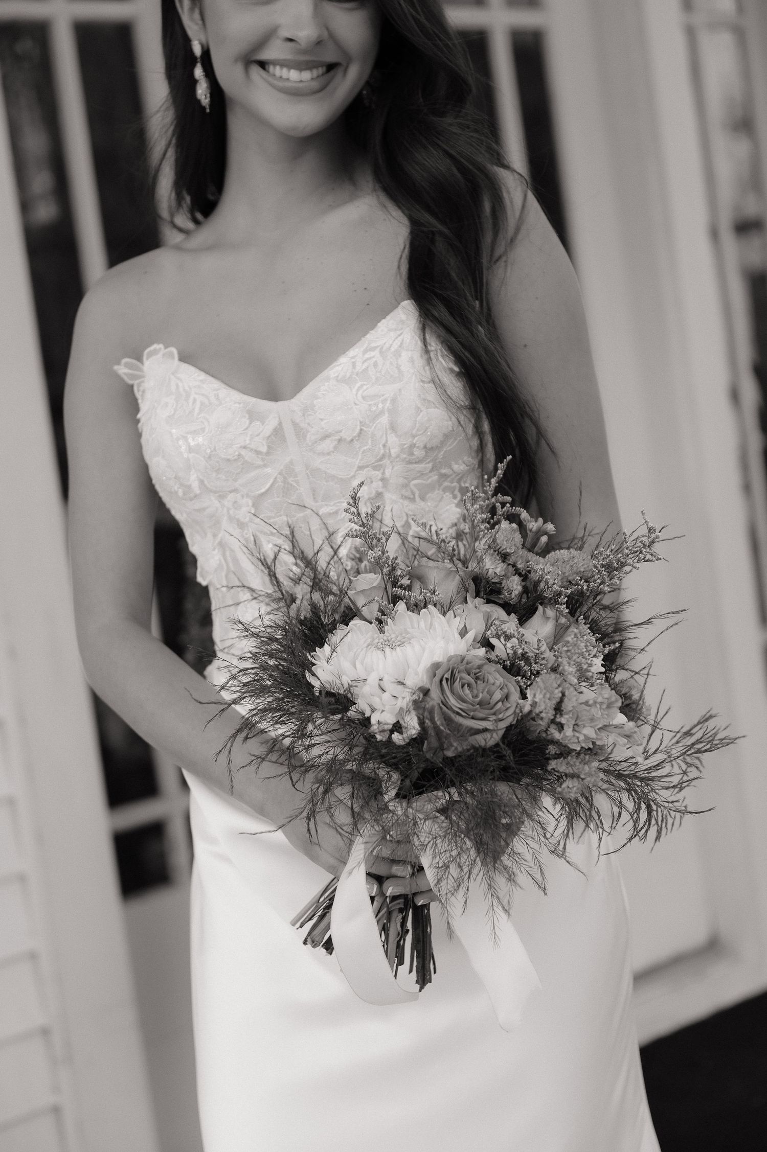Black and white portrait of bride holding an elegant floral bouquet against white architecture.