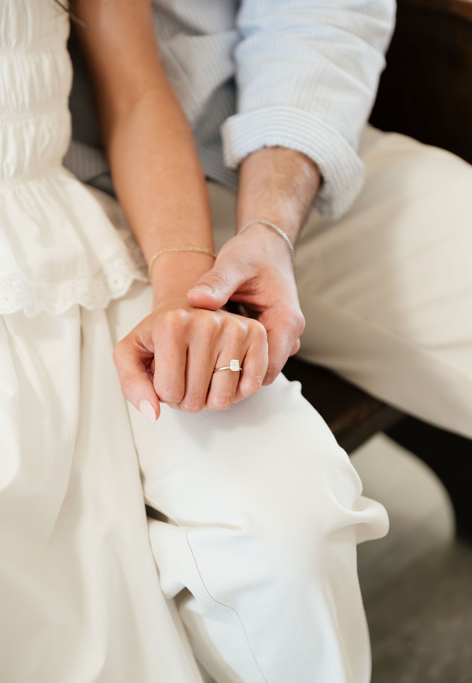 Close-up of bride and groom holding hands, showcasing a elegant solitaire engagement ring on wedding day.