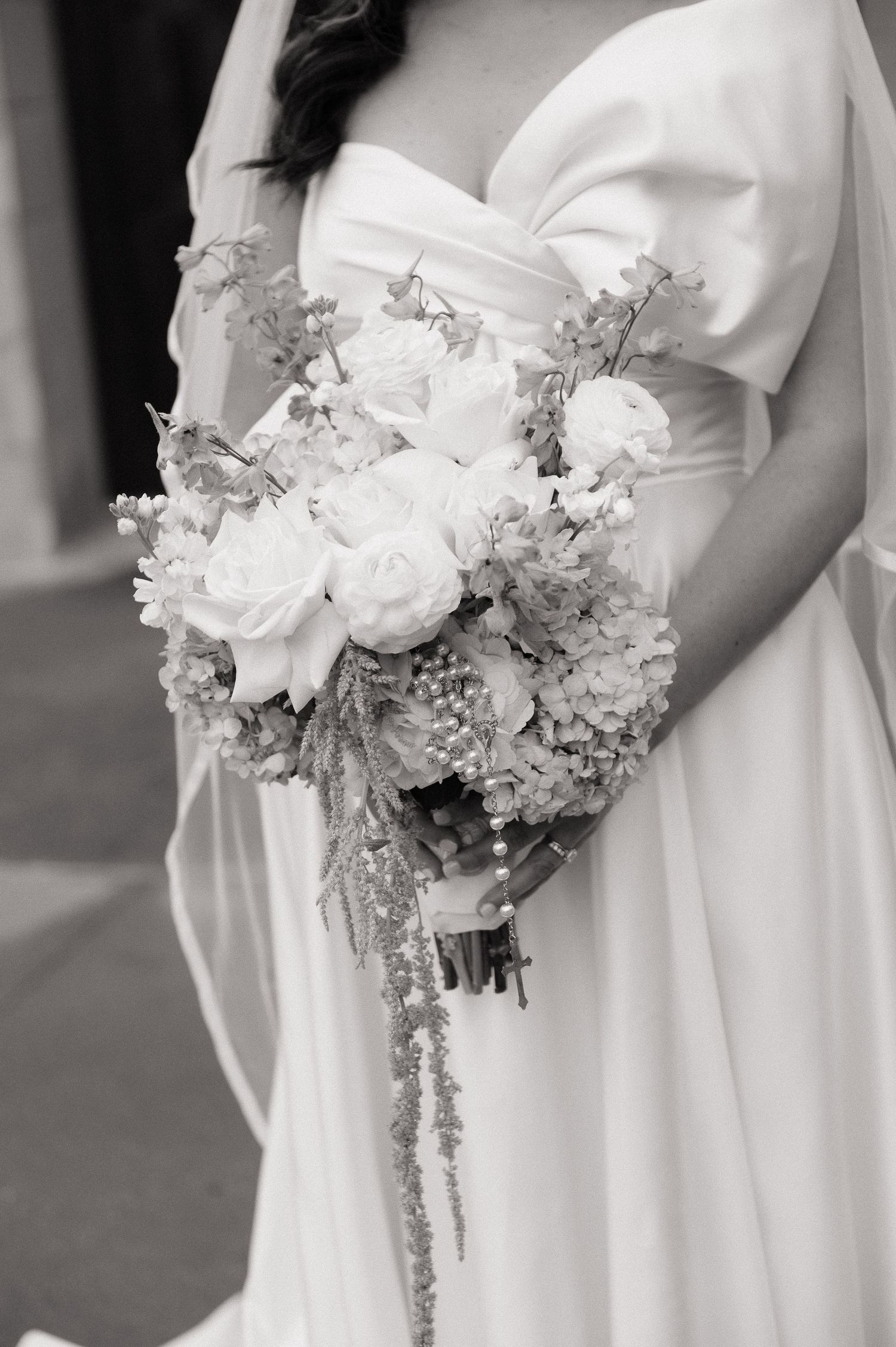 Black and white photo of a bride in a strapless gown holding a lush bouquet of roses and cascading flowers.