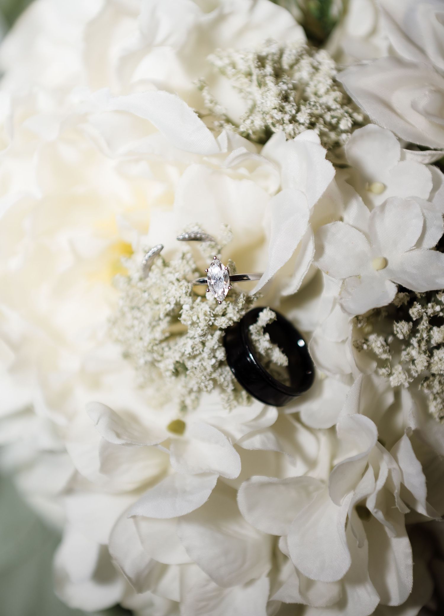 Wedding rings resting on white hydrangea and peony bouquet with delicate baby's breath flowers.