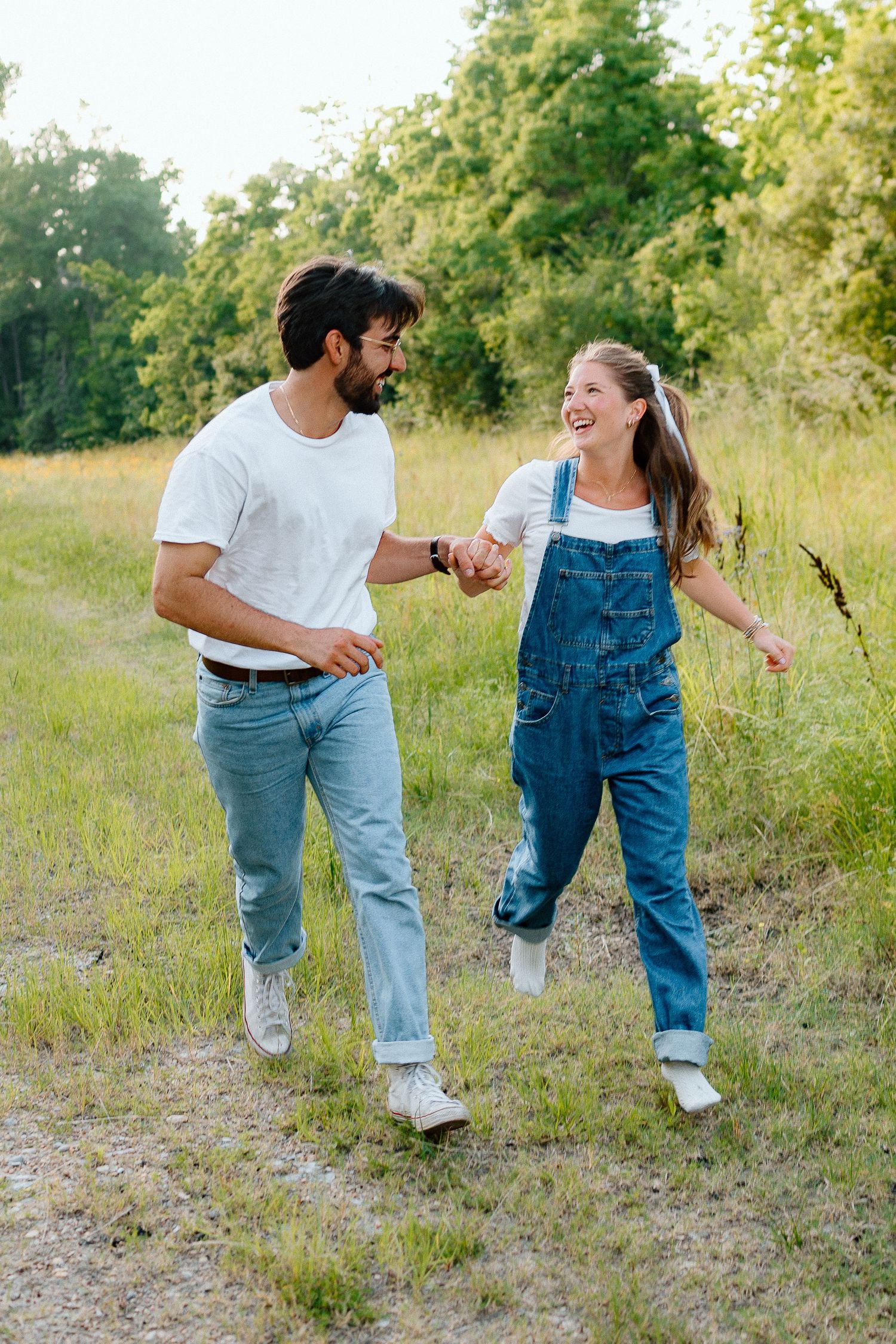Couple in casual denim and white outfits dancing together in a grassy field.