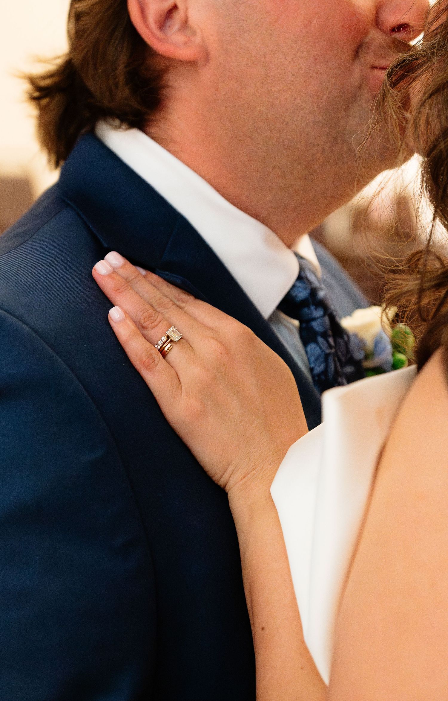 Close-up of bride's wedding ring as she places hand on groom's navy suit lapel.