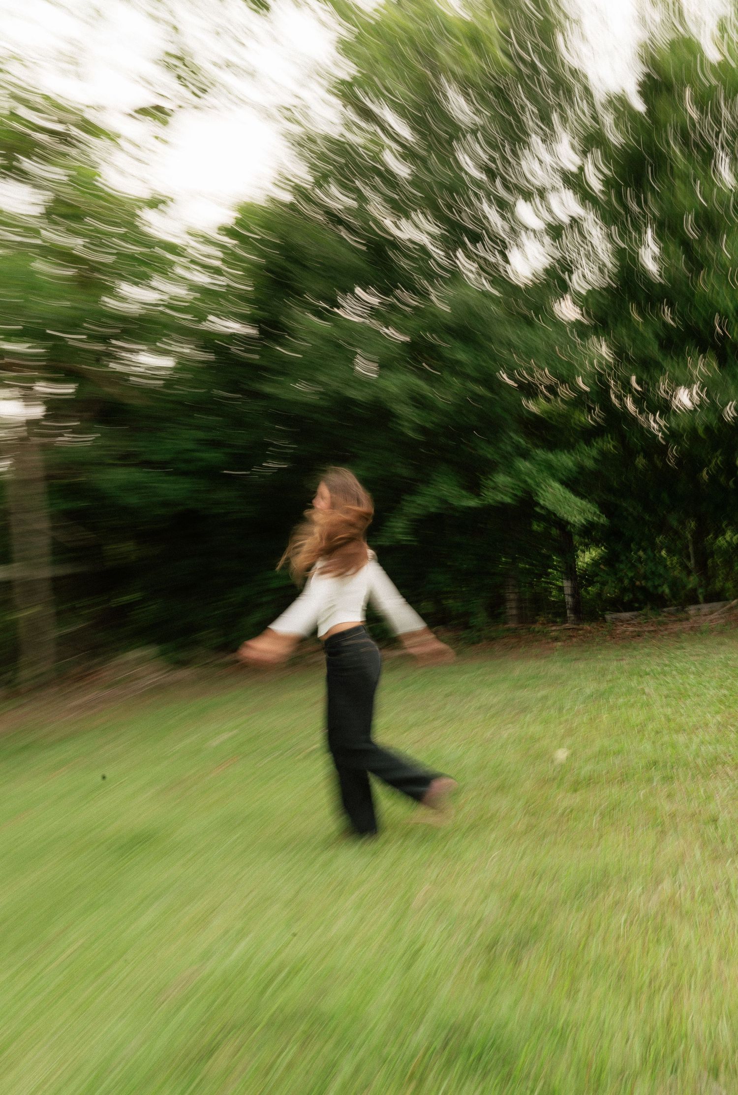 A blurred motion photo of a woman running through a lush green grassy field surrounded by trees.
