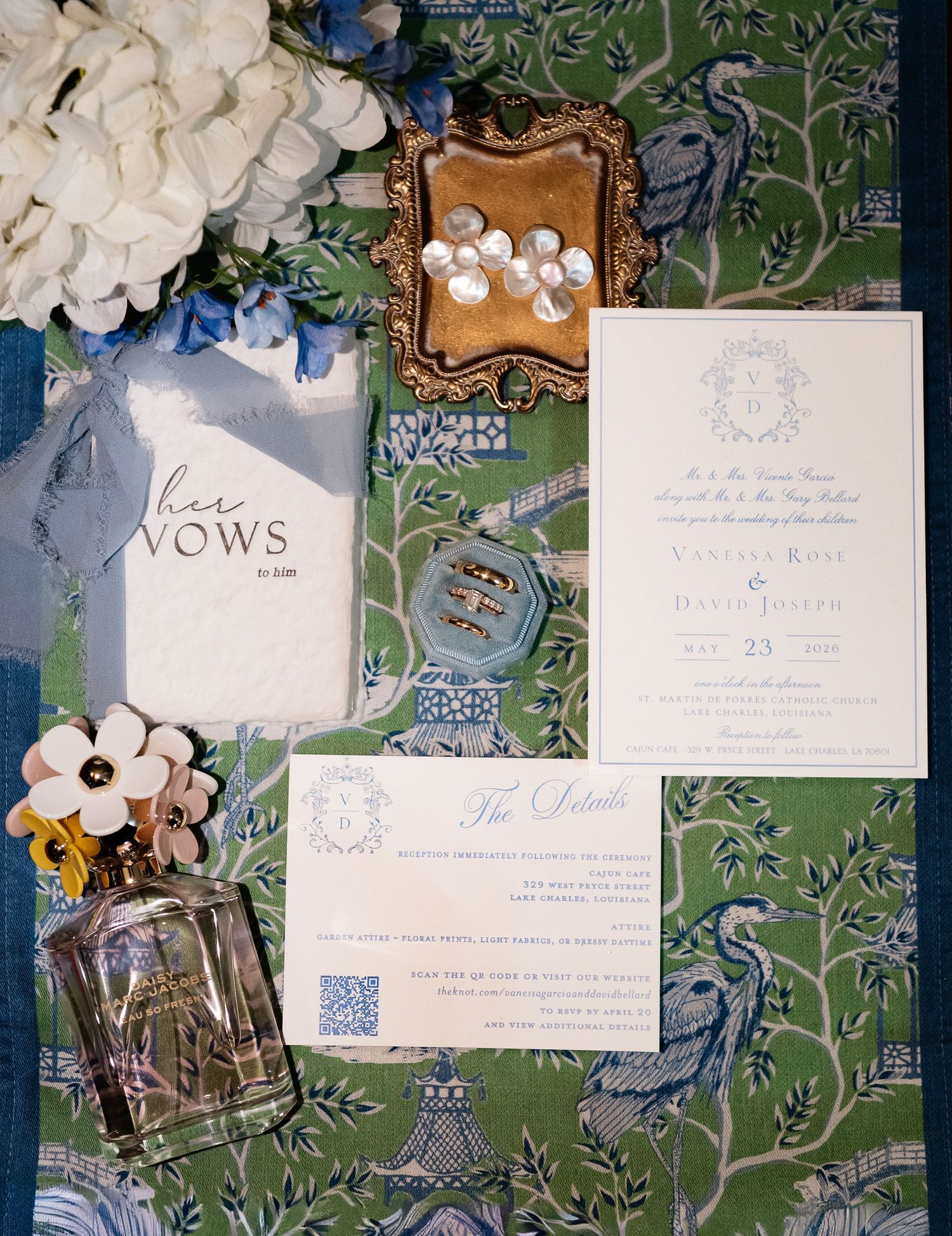 Elegant wedding invitation suite with vow booklet, rings, perfume, and floral details on green chinoiserie fabric.