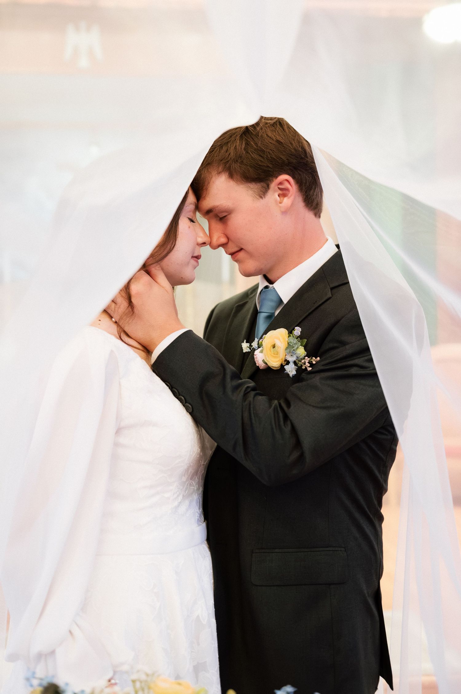 Bride and groom sharing an intimate moment under a white veil during their wedding ceremony.