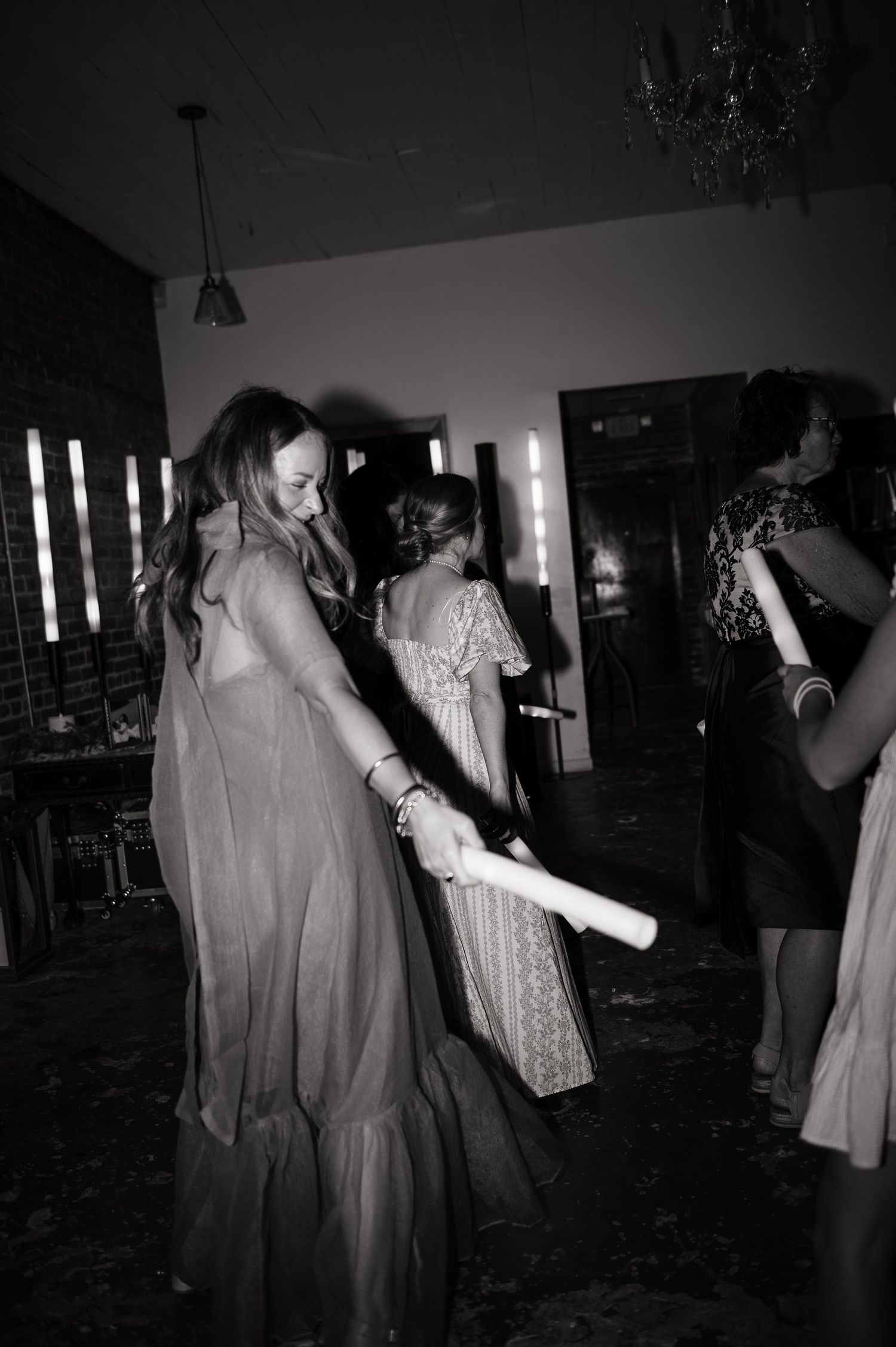 Black and white photo of wedding guests dancing with glow sticks at lively reception celebration.