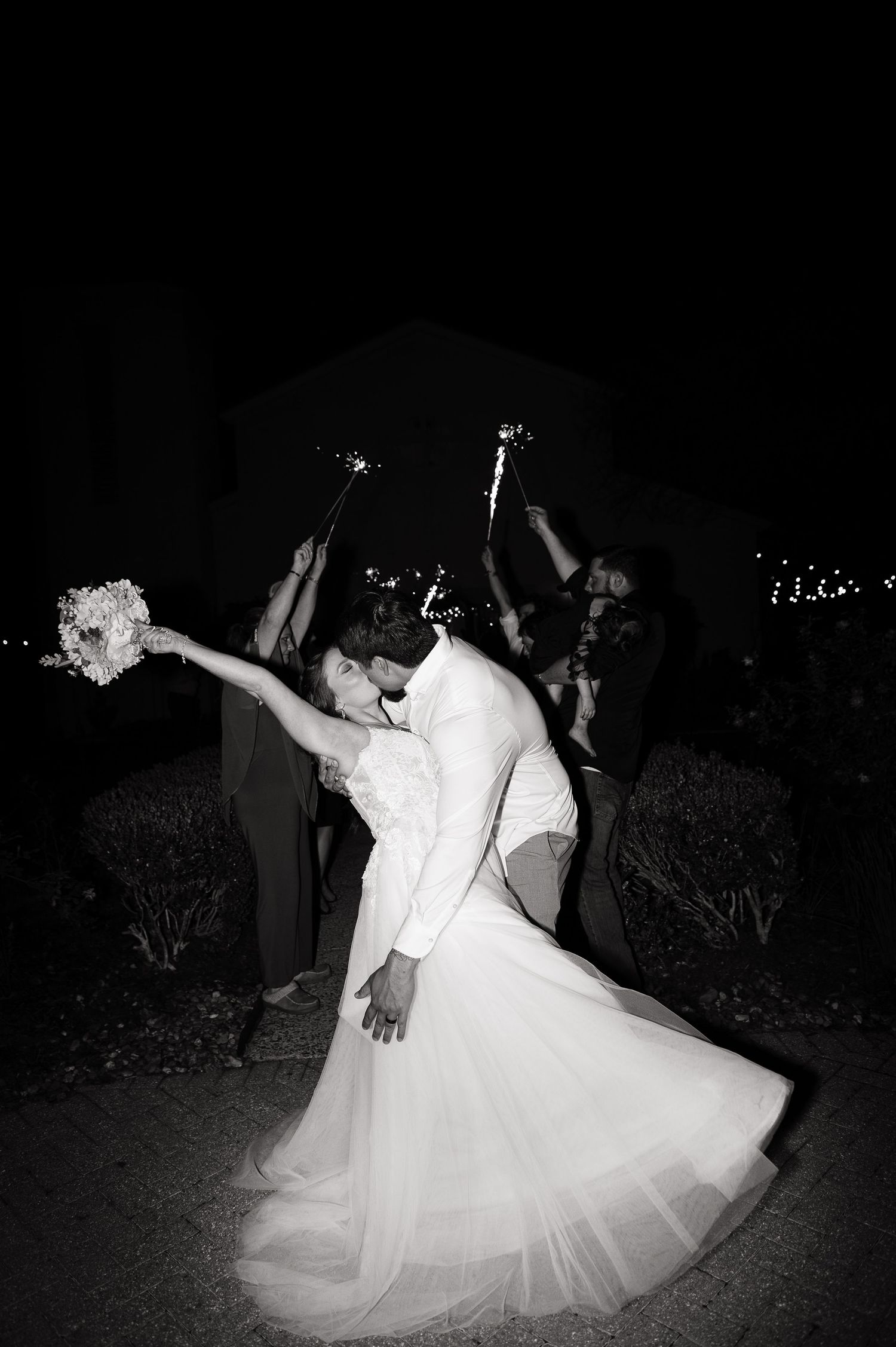 Bride and groom share a romantic dip kiss surrounded by sparklers at their outdoor wedding reception.