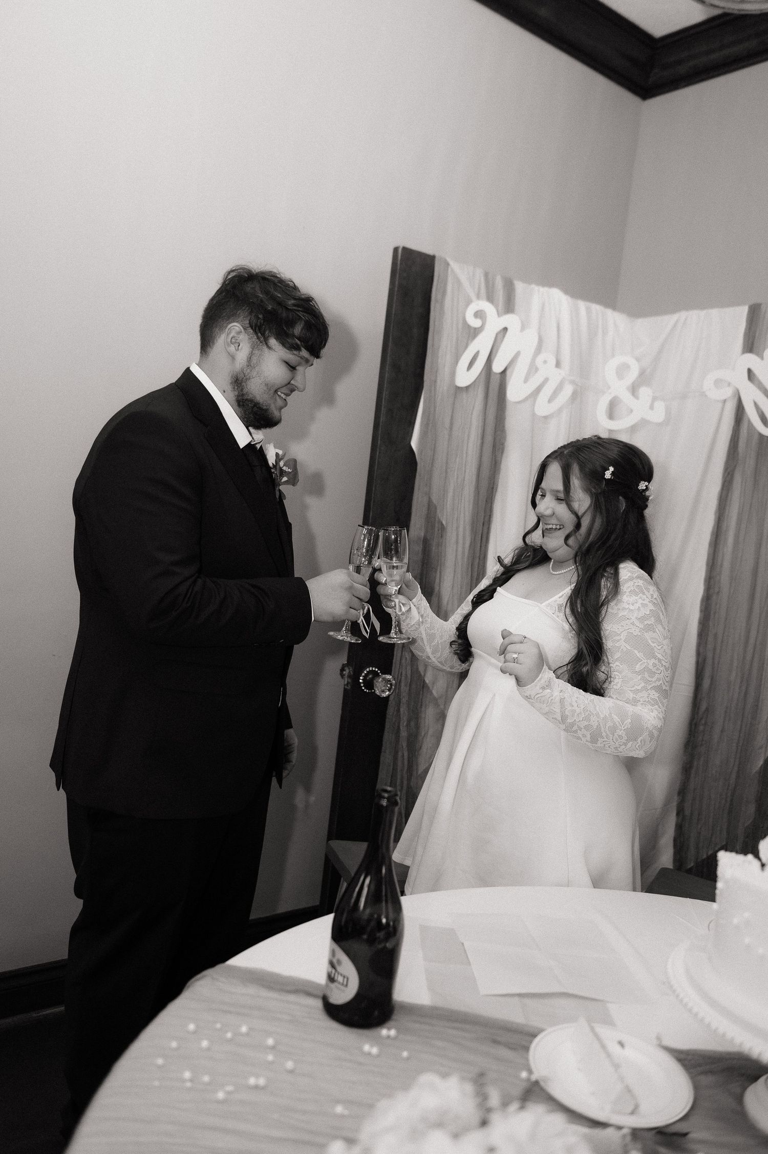 Black and white photo of a bride and groom toasting with champagne glasses at their wedding reception.