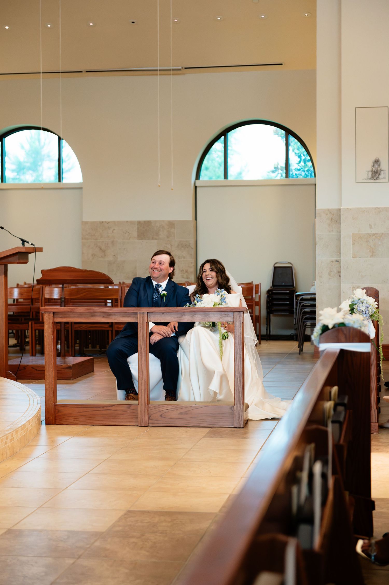 Bride and groom seated together at the altar during their wedding ceremony inside a modern church.