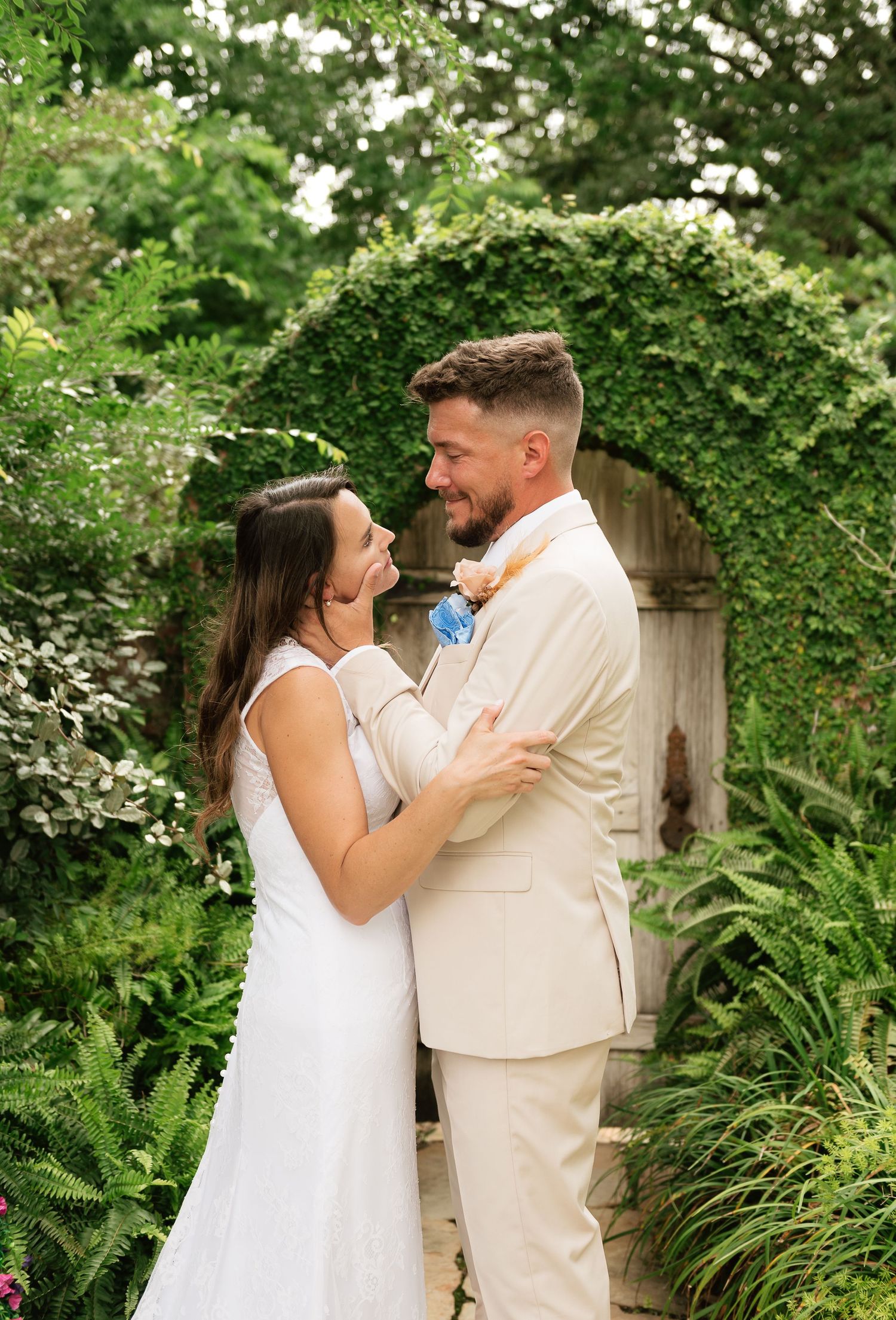 A bride and groom embrace and smile at each other in front of a lush ivy-covered garden archway.