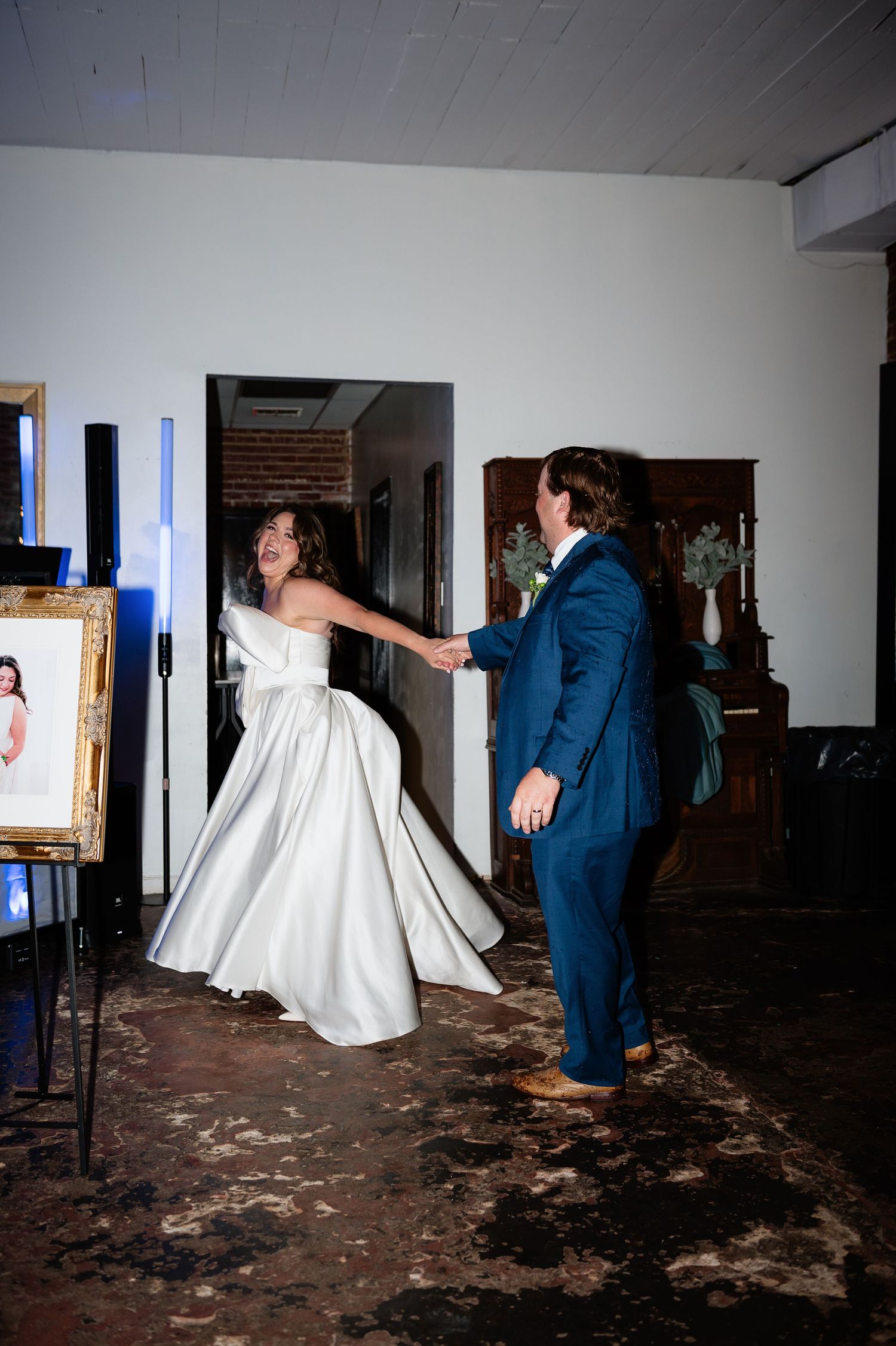 Bride in white strapless gown and groom in blue suit share first dance at wedding reception.