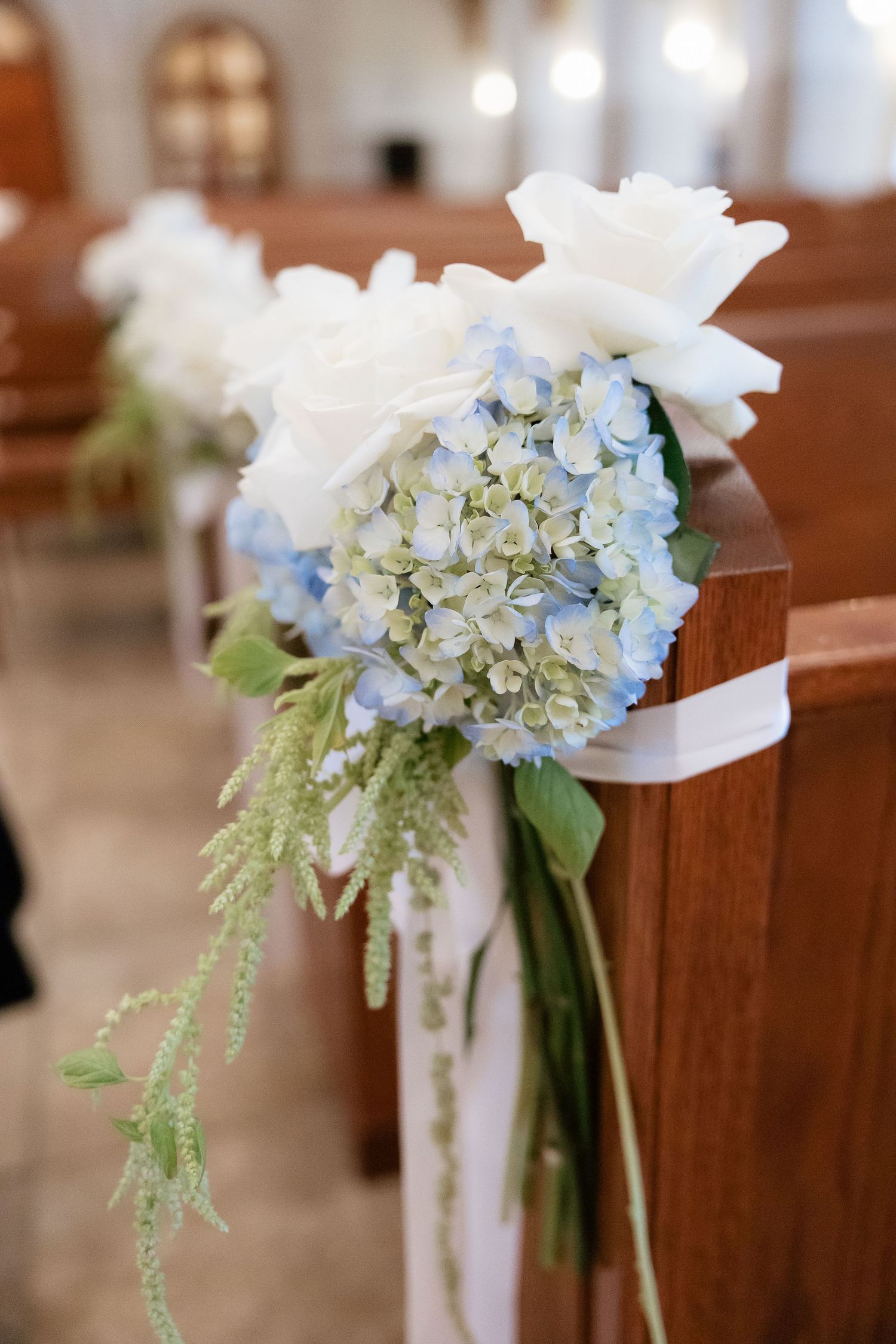 Blue hydrangea and white rose wedding pew arrangement with ribbon in a church.