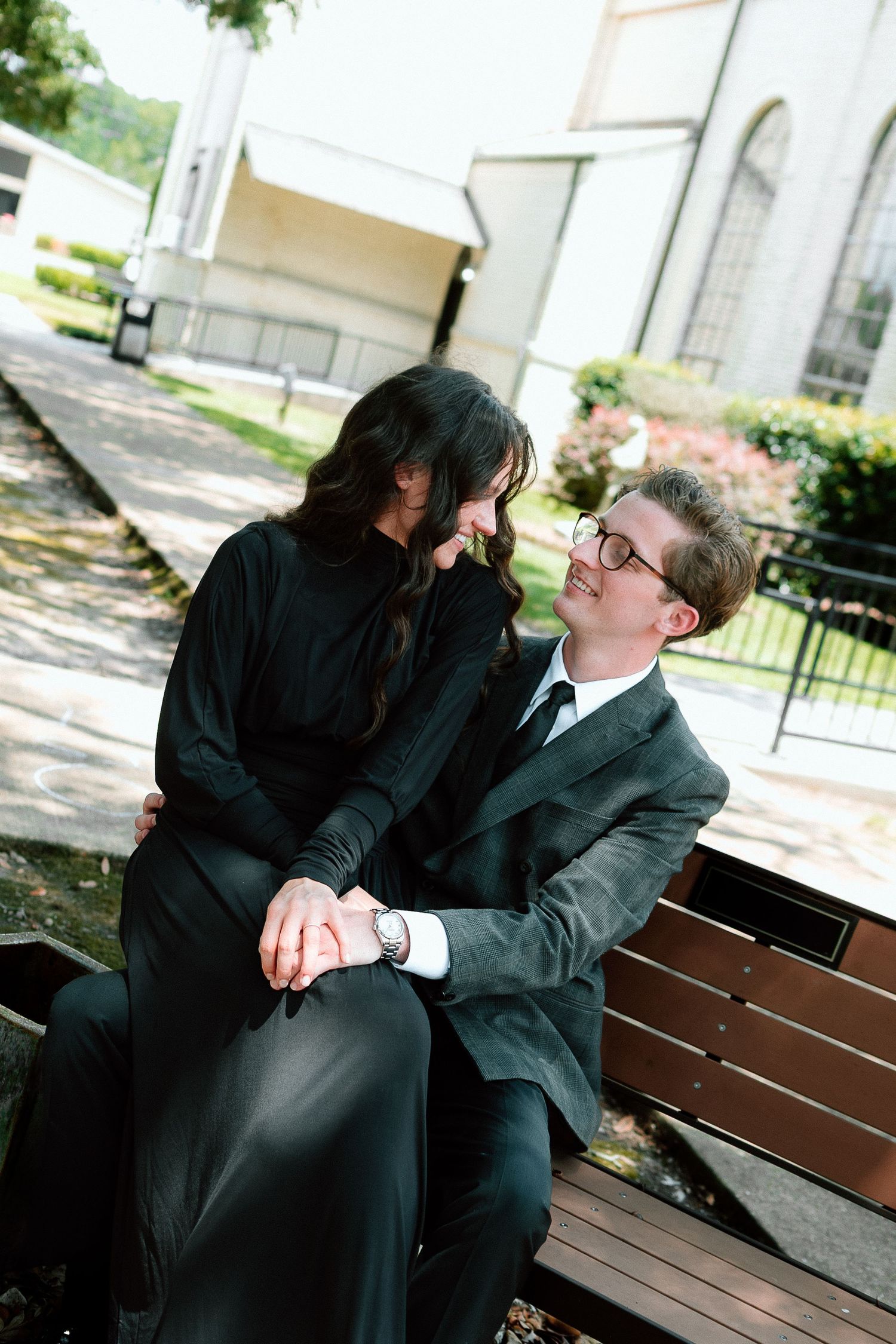 Couple shares intimate moments on wooden bench in formal attire.