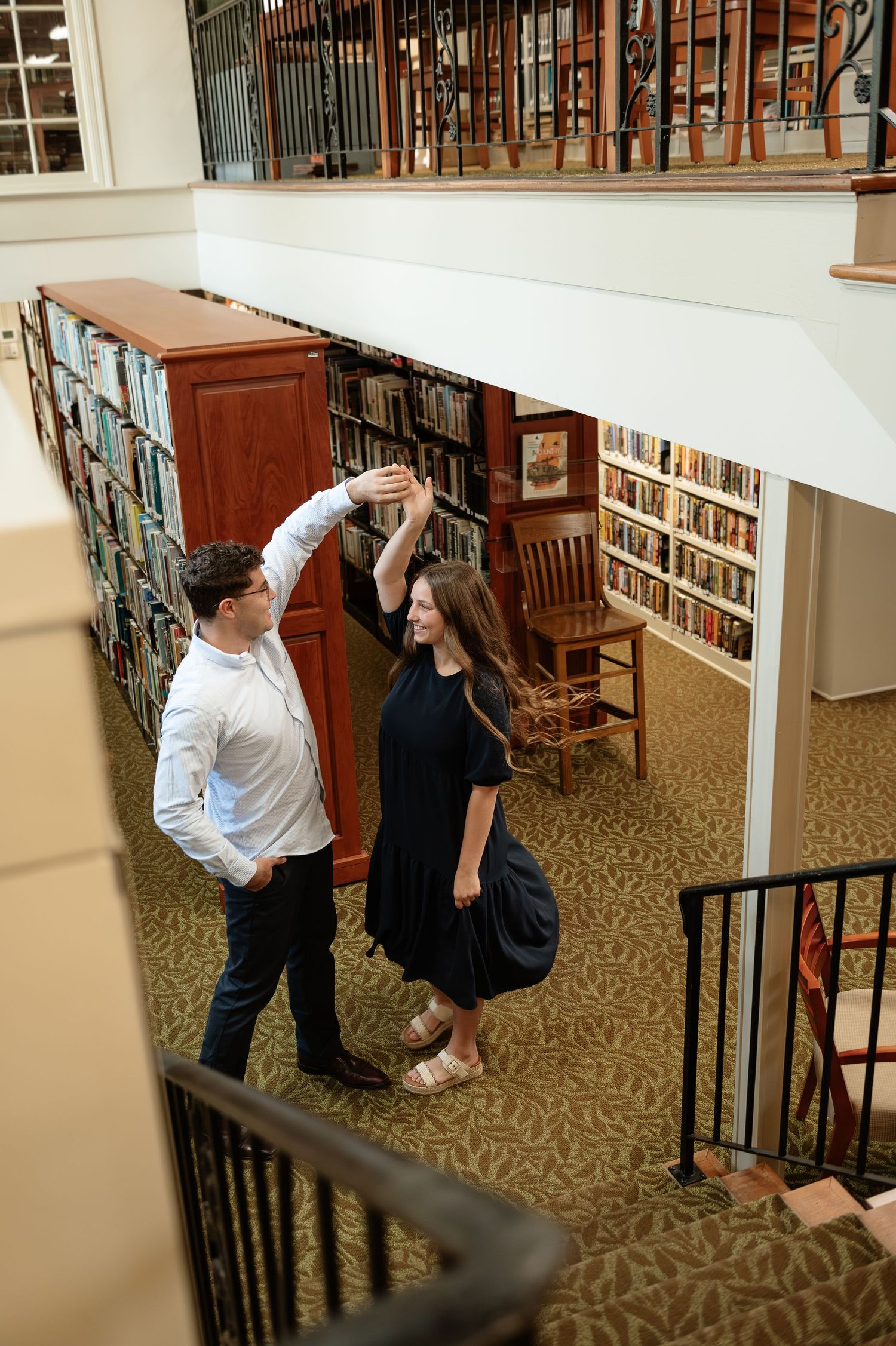 Couple dancing together in a charming two-story bookstore library with wooden shelves full of books.