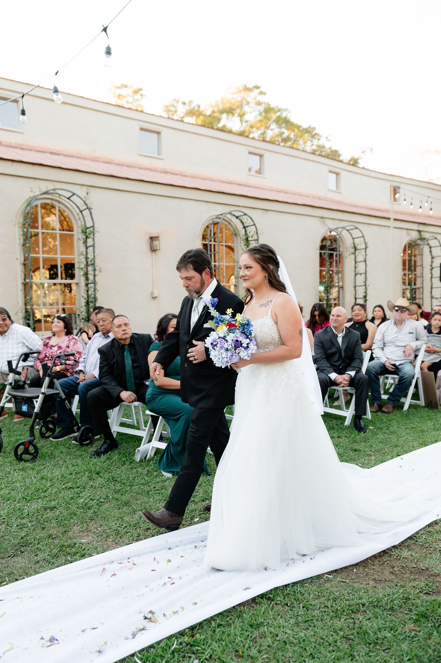 Bride and groom walking down the aisle at an outdoor wedding ceremony, bride holding purple bouquet.