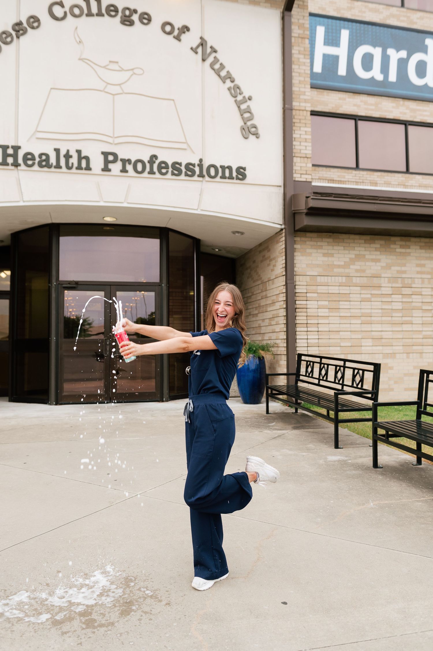 Nursing graduate celebrating by popping champagne outside College of Nursing and Health Professions.