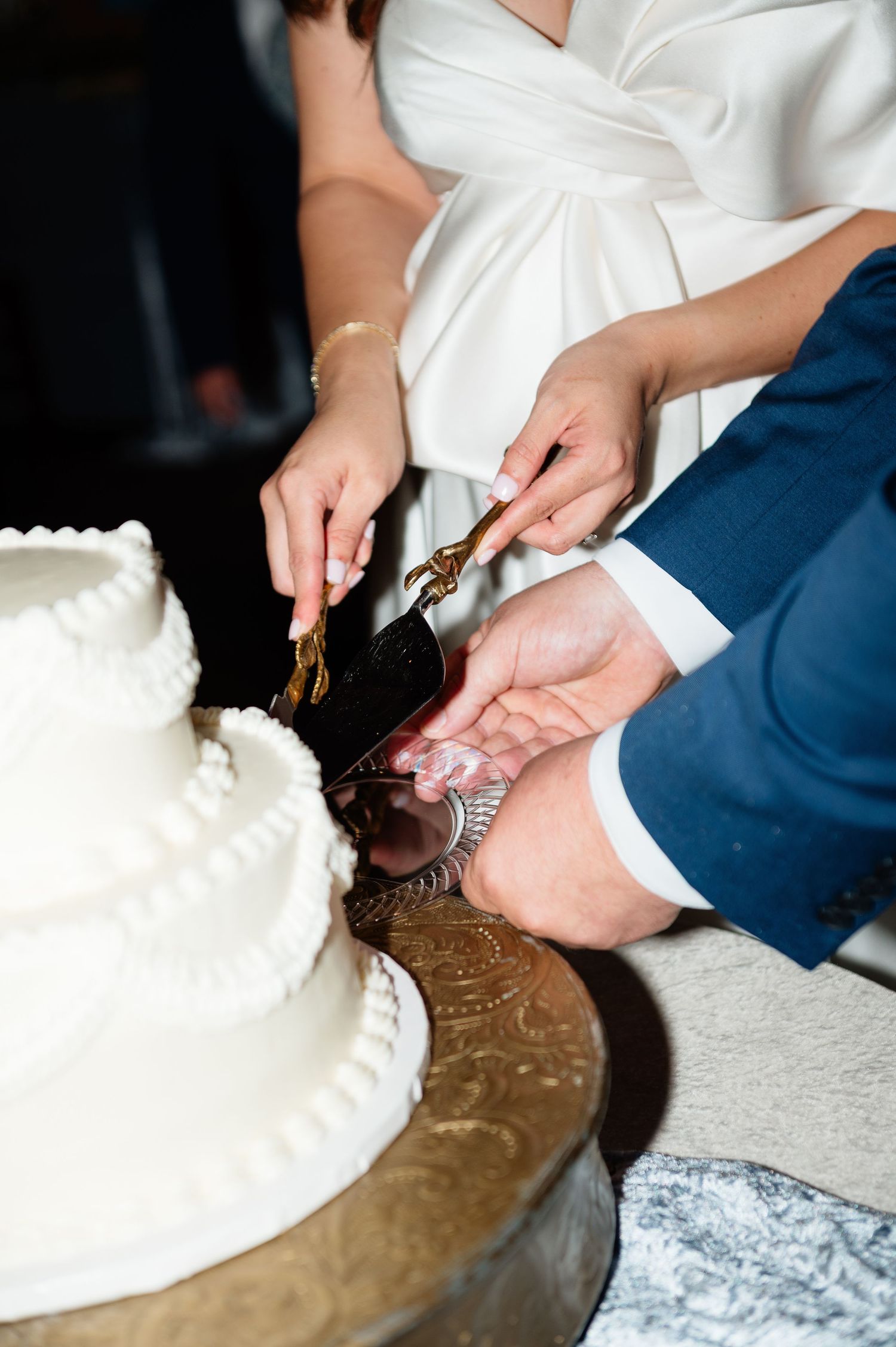 Bride and groom cutting white three-tier wedding cake with ornate gold cake server.