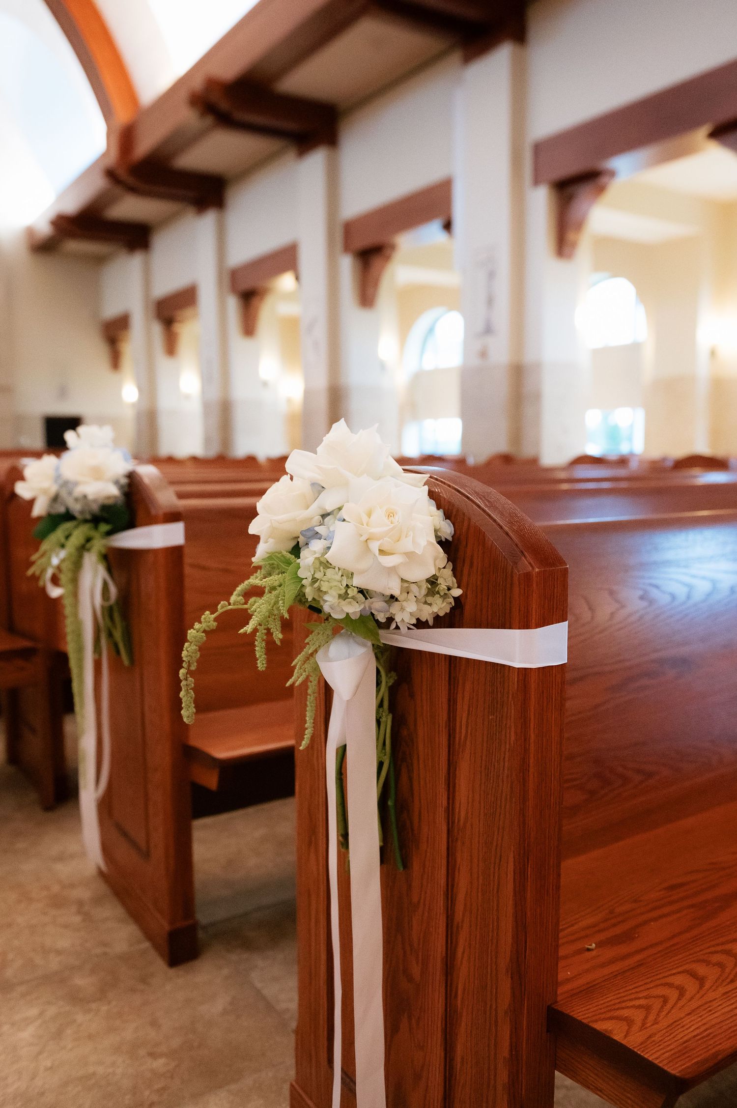 White floral bouquets with ribbon accents decorating wooden church pews for an elegant wedding ceremony.