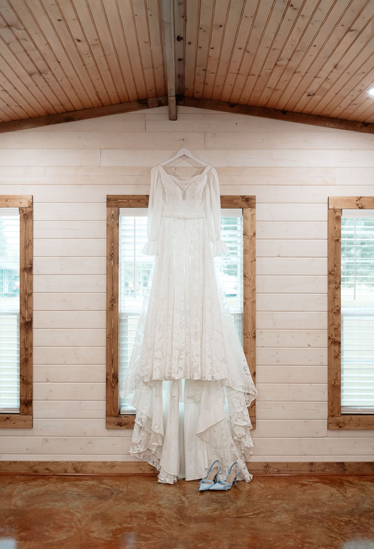 White lace wedding dress with long sleeves hanging in a rustic barn venue with wood walls and vaulted ceiling.