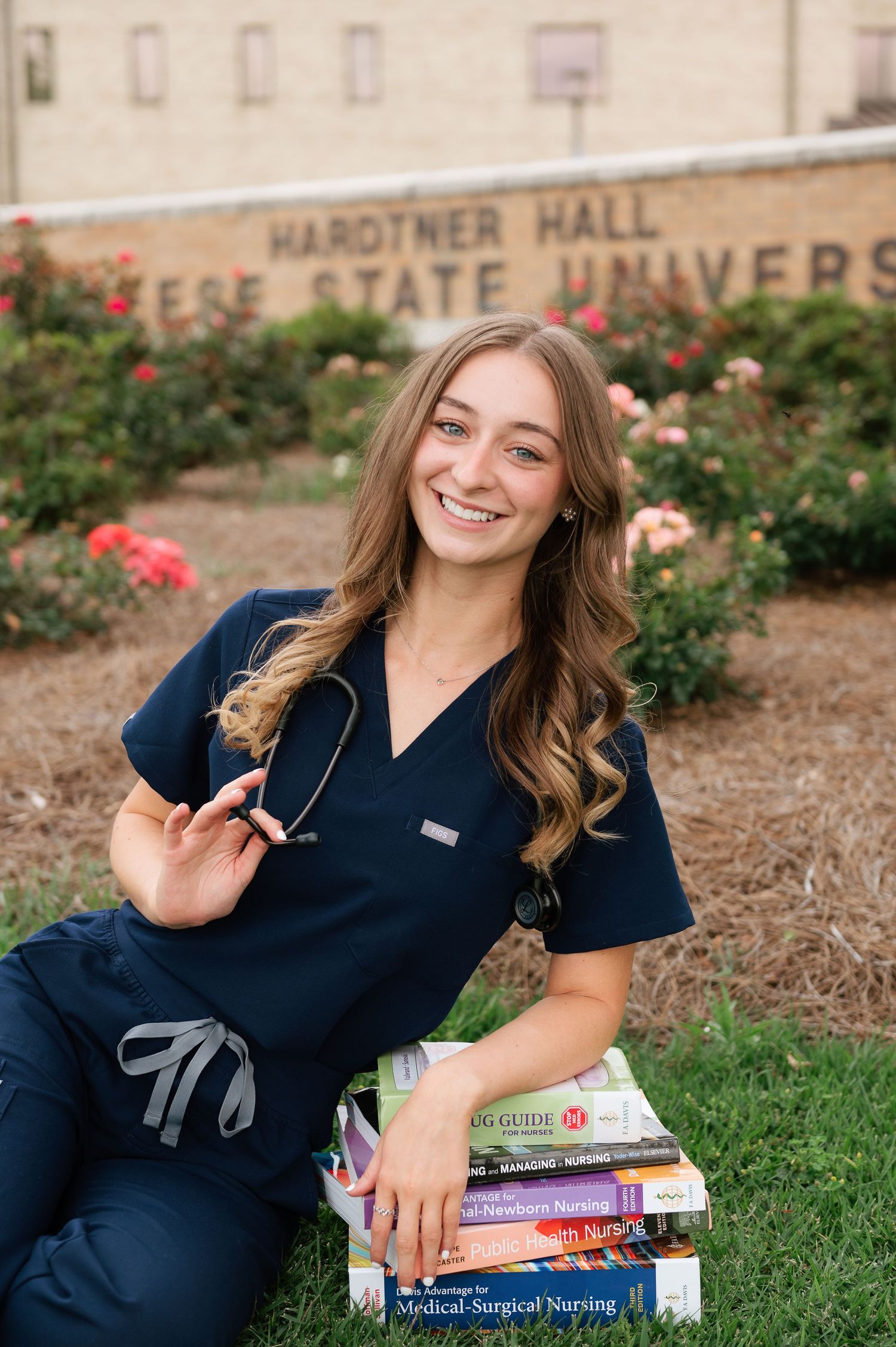 Nursing student in scrubs sitting on textbooks outside Hardtner Hall at Louisiana State University.