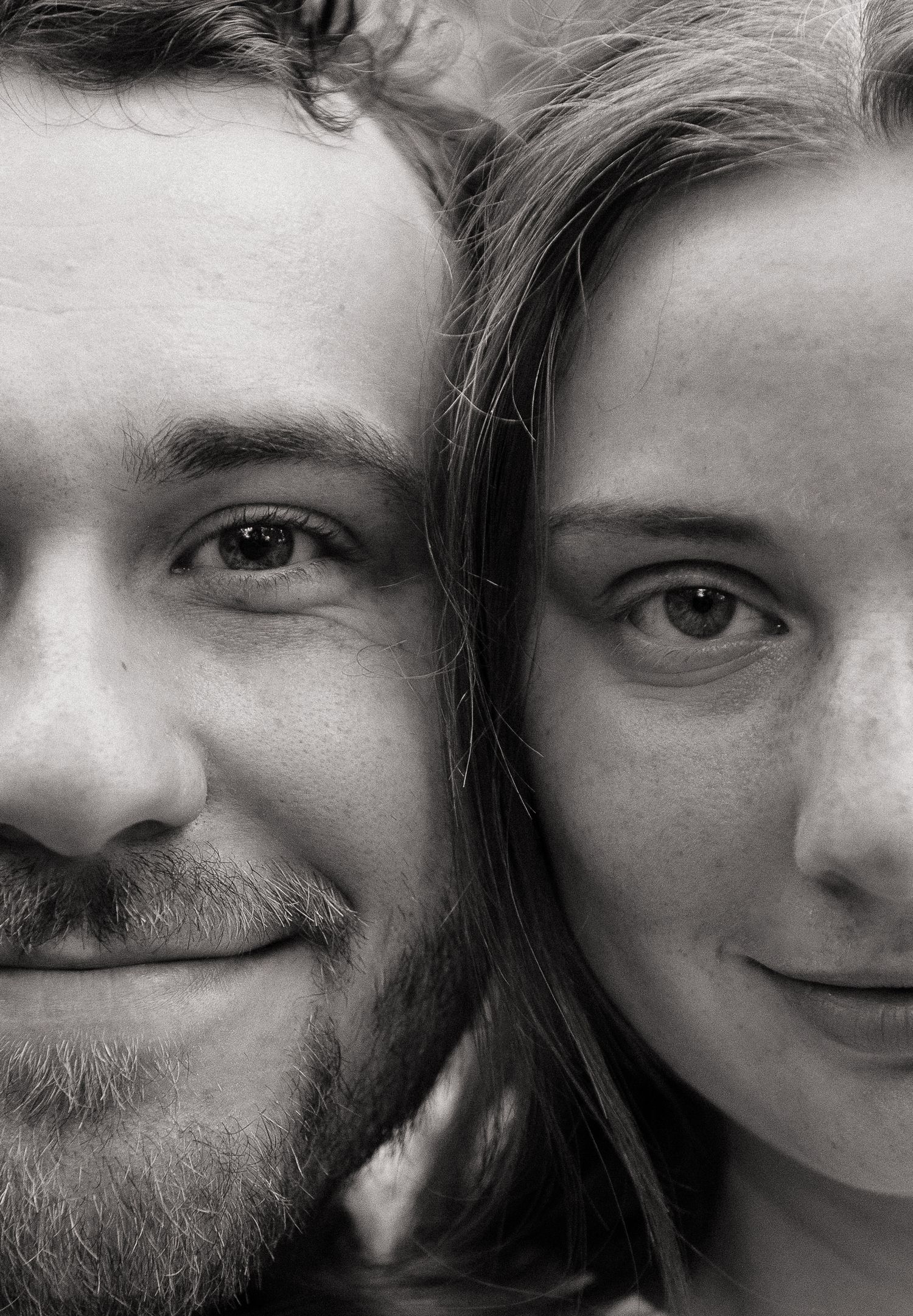 Black and white close-up portrait of a smiling man with stubble and a young woman with freckles cheek to cheek.