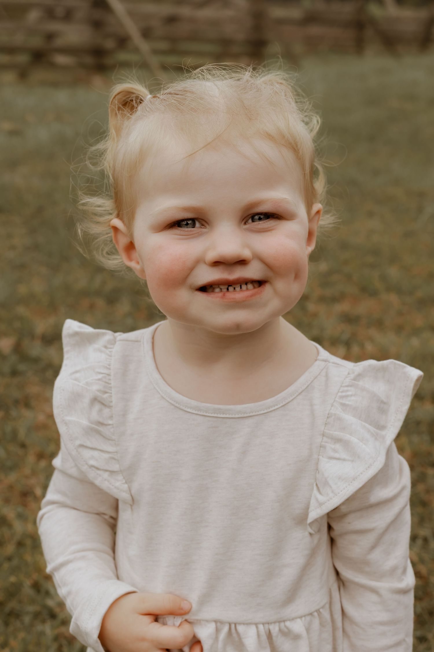 Close-up portrait of a young child wearing a white ruffled dress smiling at the camera.