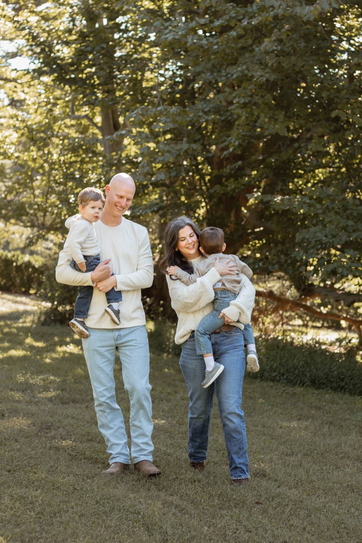 Family enjoying a sunny autumn day outdoors with their young children in matching white sweaters.