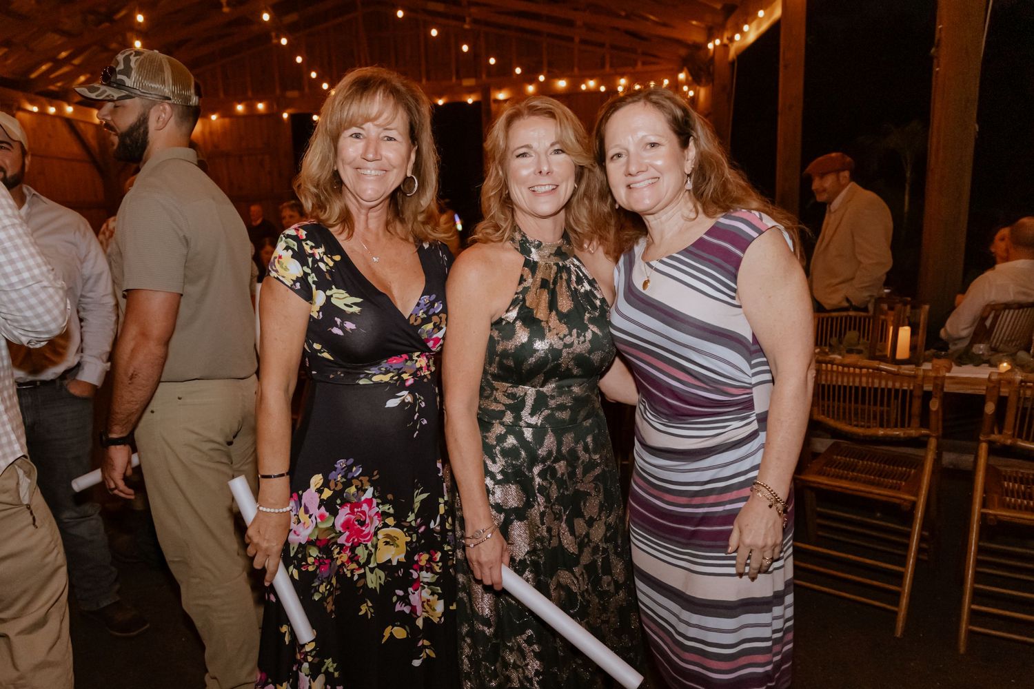 Three women smiling and posing together at an elegant indoor event with string lights in the background.