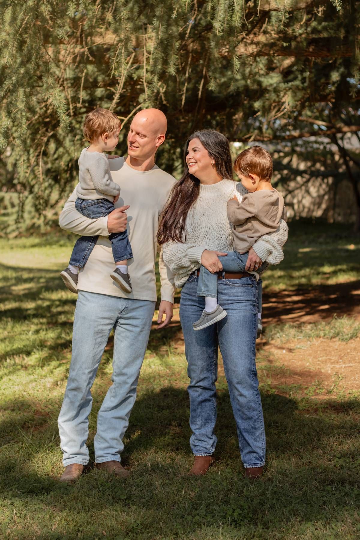 Family of four in coordinated casual wear poses together in a sunlit garden setting.