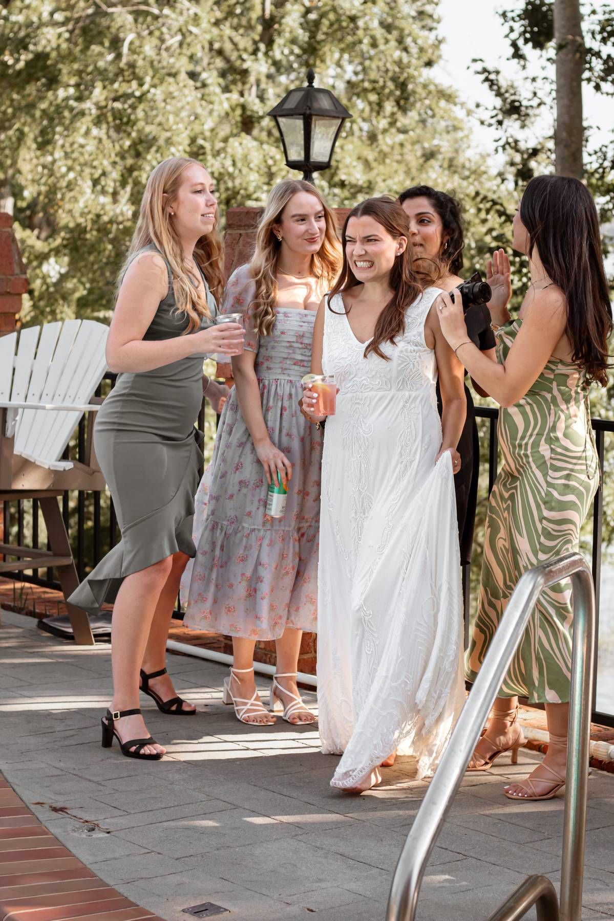 Wedding party members in floral dresses share laughs on outdoor patio.