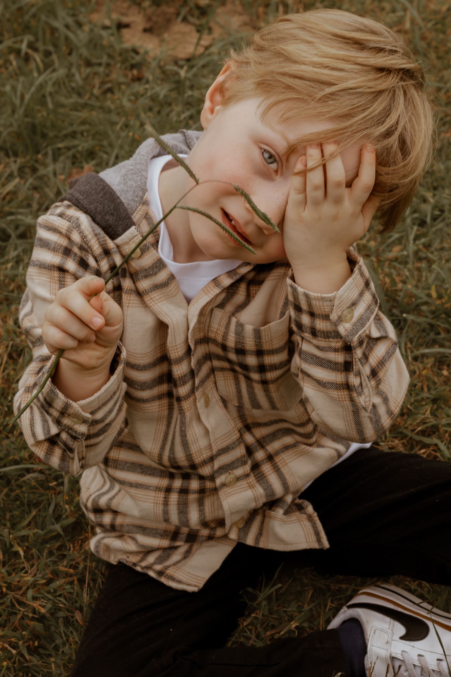 Child in plaid shirt lies on grass during outdoor autumn photoshoot.
