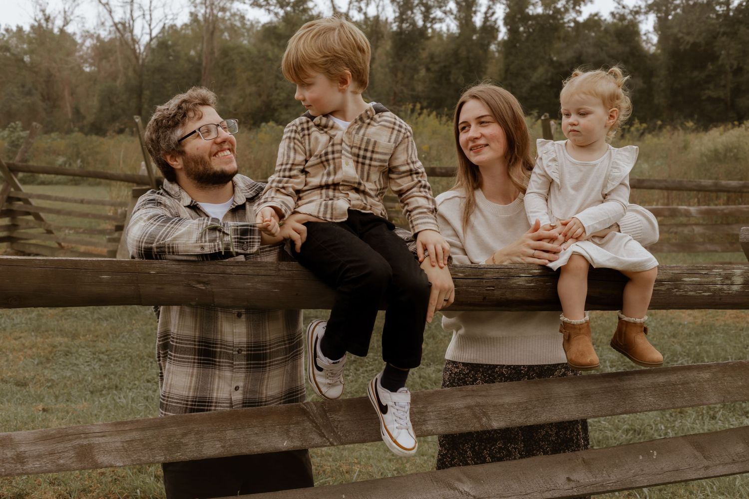 Family members sit and play on wooden fence during outdoor photo session.