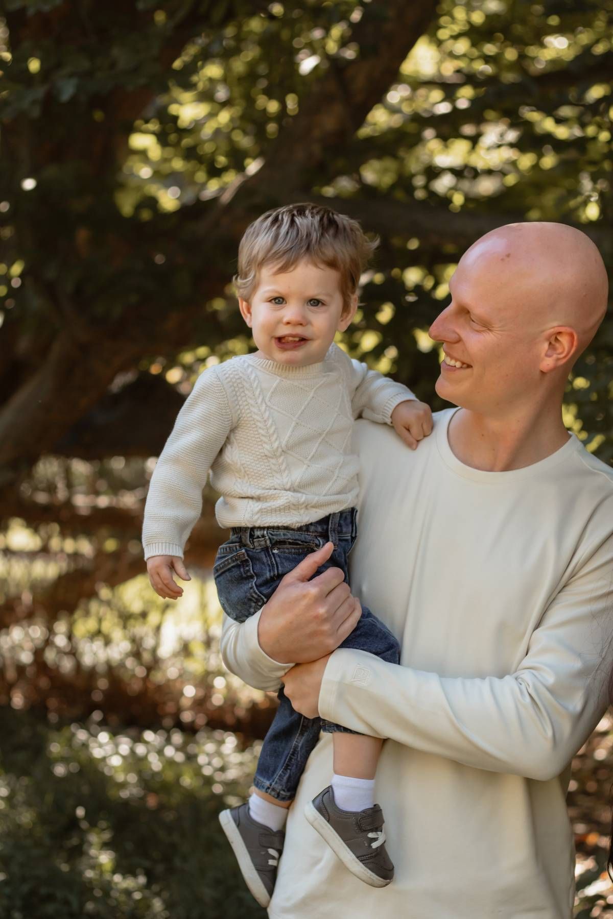 Parent and toddler share a joyful moment outdoors wearing matching cream sweaters.
